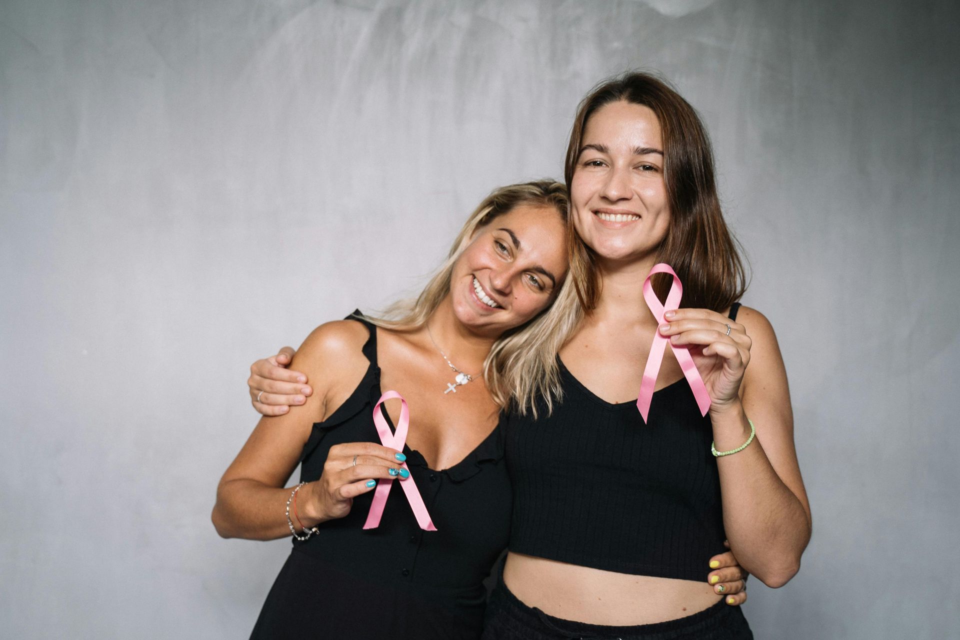 Two women are standing next to each other holding pink ribbons.