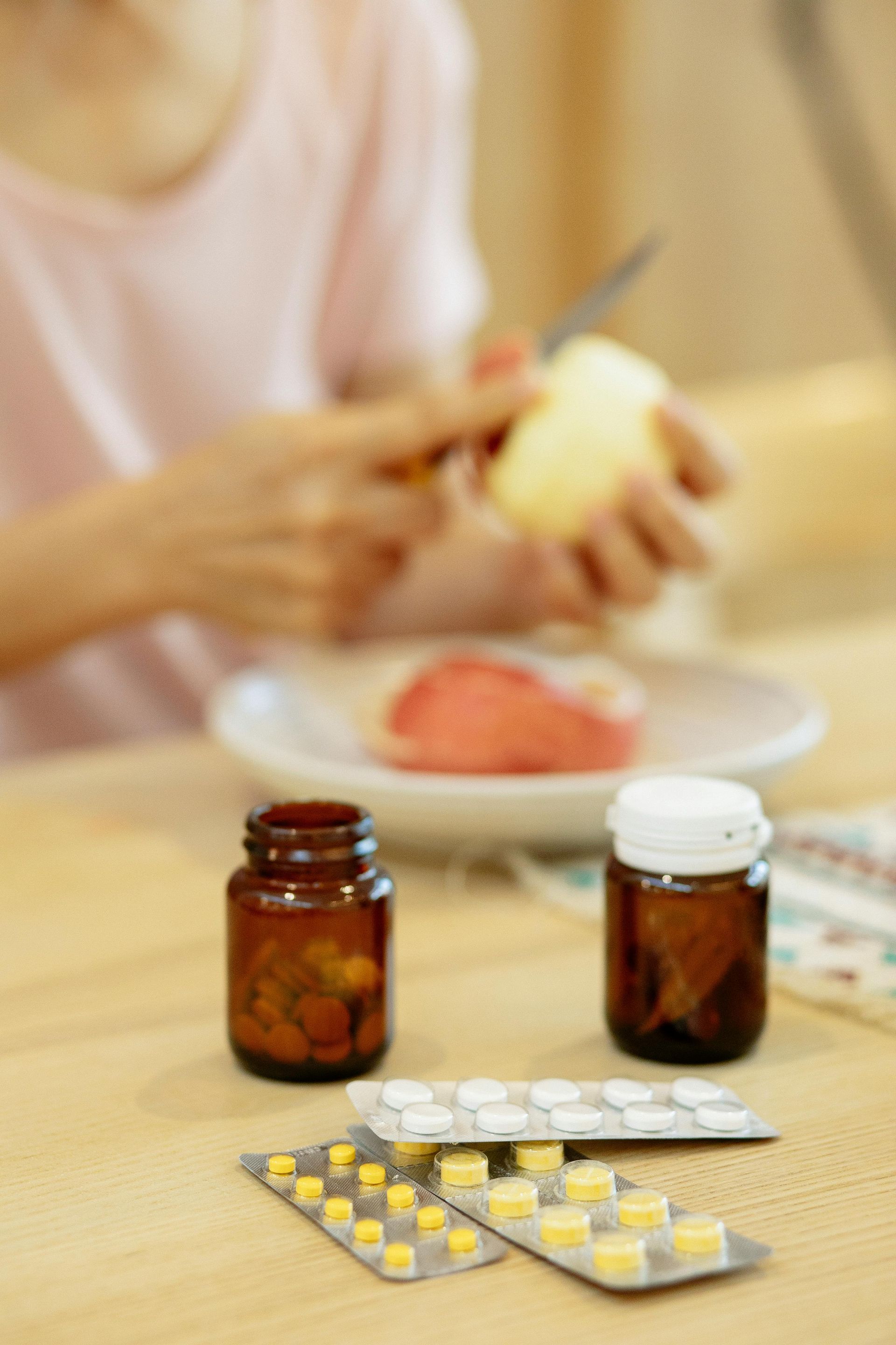 A woman is sitting at a table with bottles of pills and a plate of food.