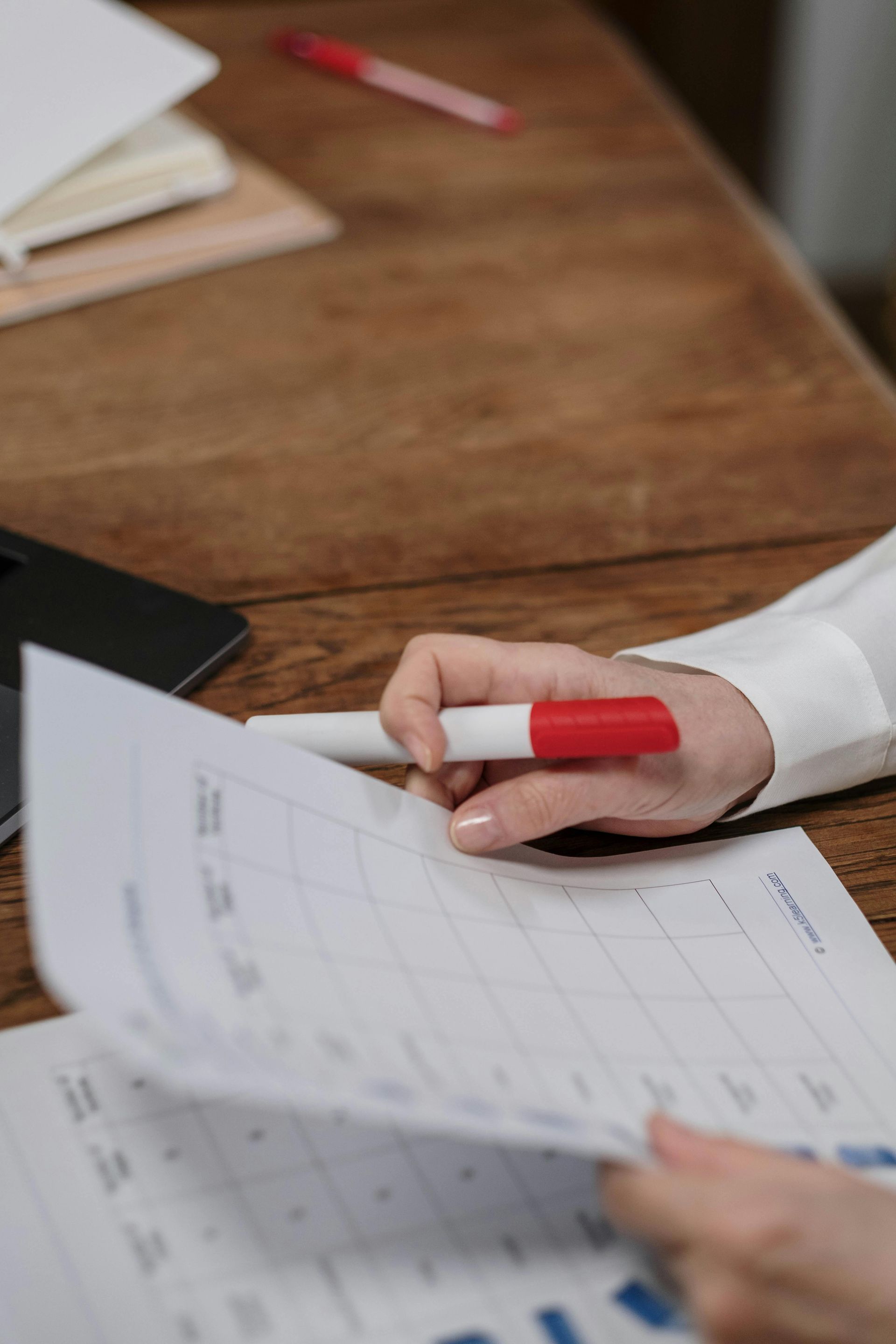 A person is holding a red and white pen over a piece of paper.