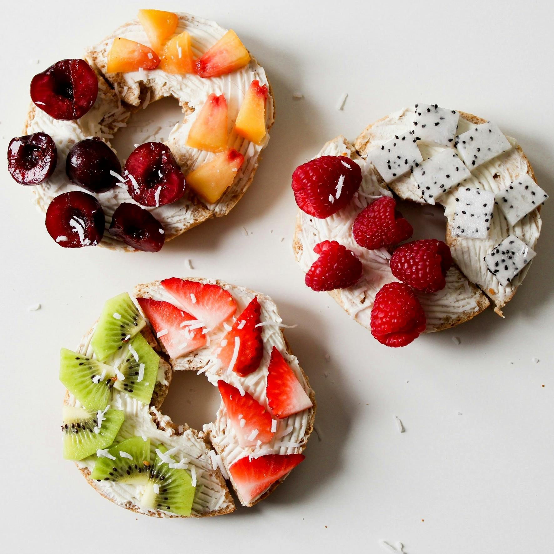 Three bagels with different toppings including strawberries kiwi and dragon fruit