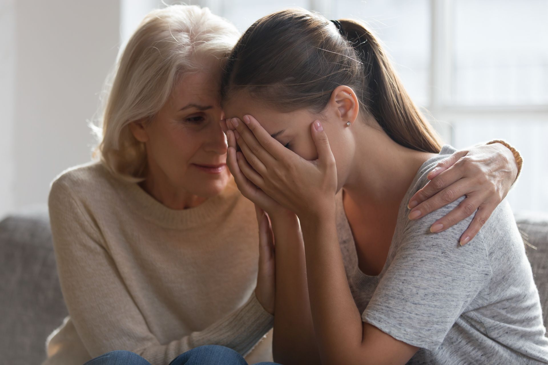 A woman is comforting another woman who is crying on a couch.