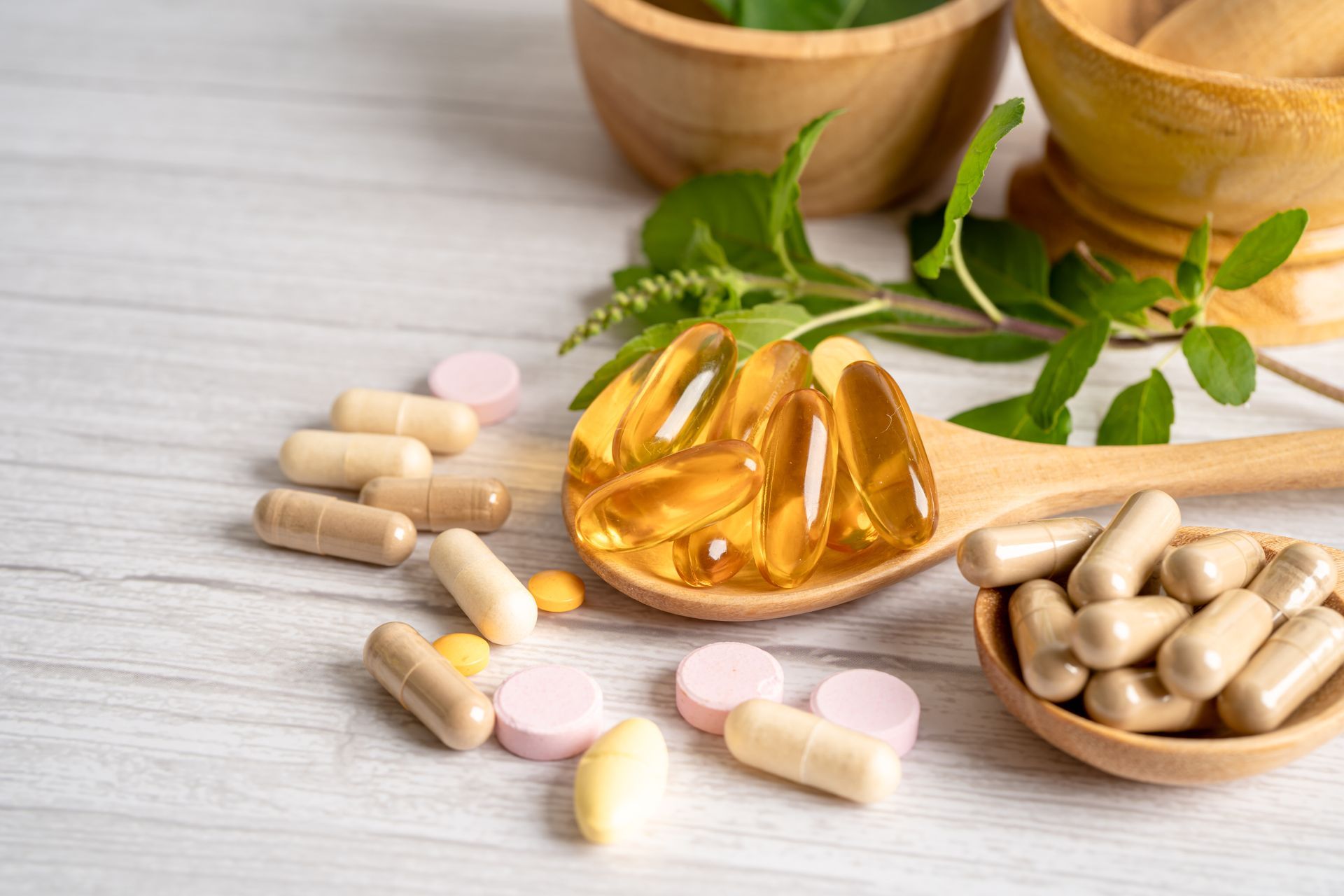 A wooden spoon filled with pills and a bowl of pills on a table.