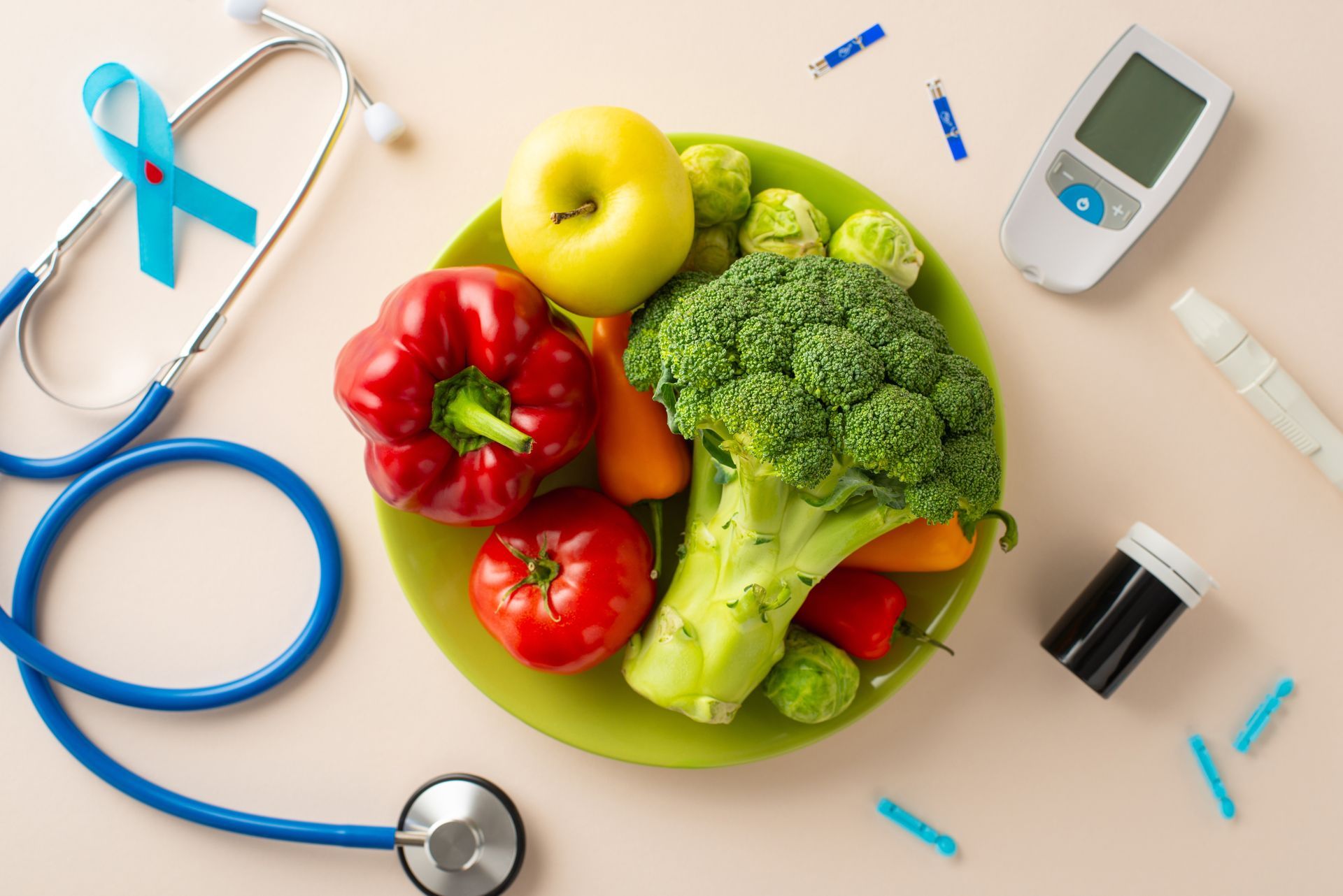 A plate of fruits and vegetables next to a stethoscope and a diabetes monitor.
