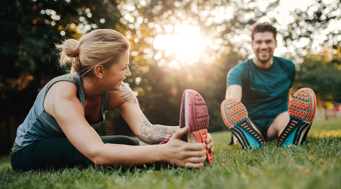 A man and a woman are sitting on the grass stretching their legs.