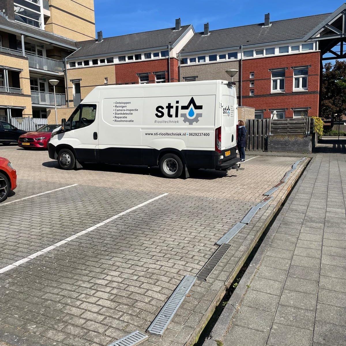 Een witte STIHL-servicebus staat geparkeerd op een straat met kinderkopjes, naast bakstenen gebouwen.