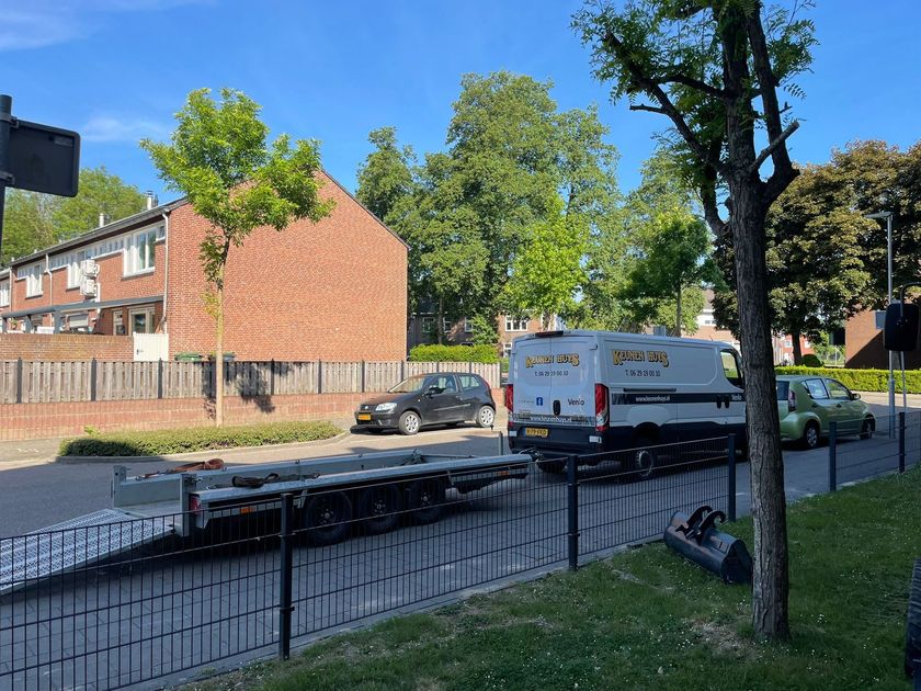 Rustige woonstraat met een witte bestelbus, een geparkeerde auto en bakstenen huizen achter een zwart hek.