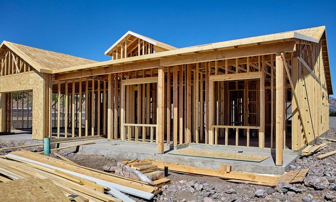 House under construction, wooden frame, against a clear blue sky.