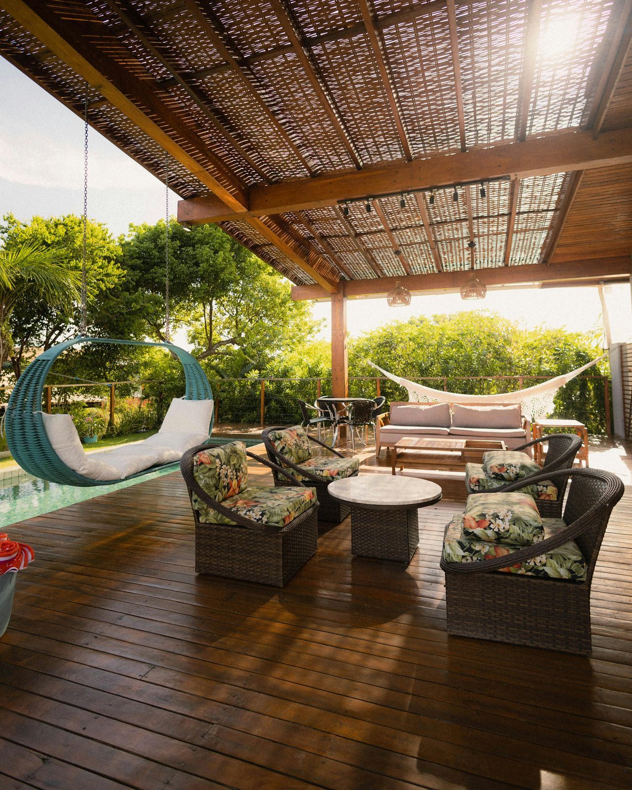 Patio with a hanging chair, seating area with floral cushions, and a hammock, under a wooden pergola.