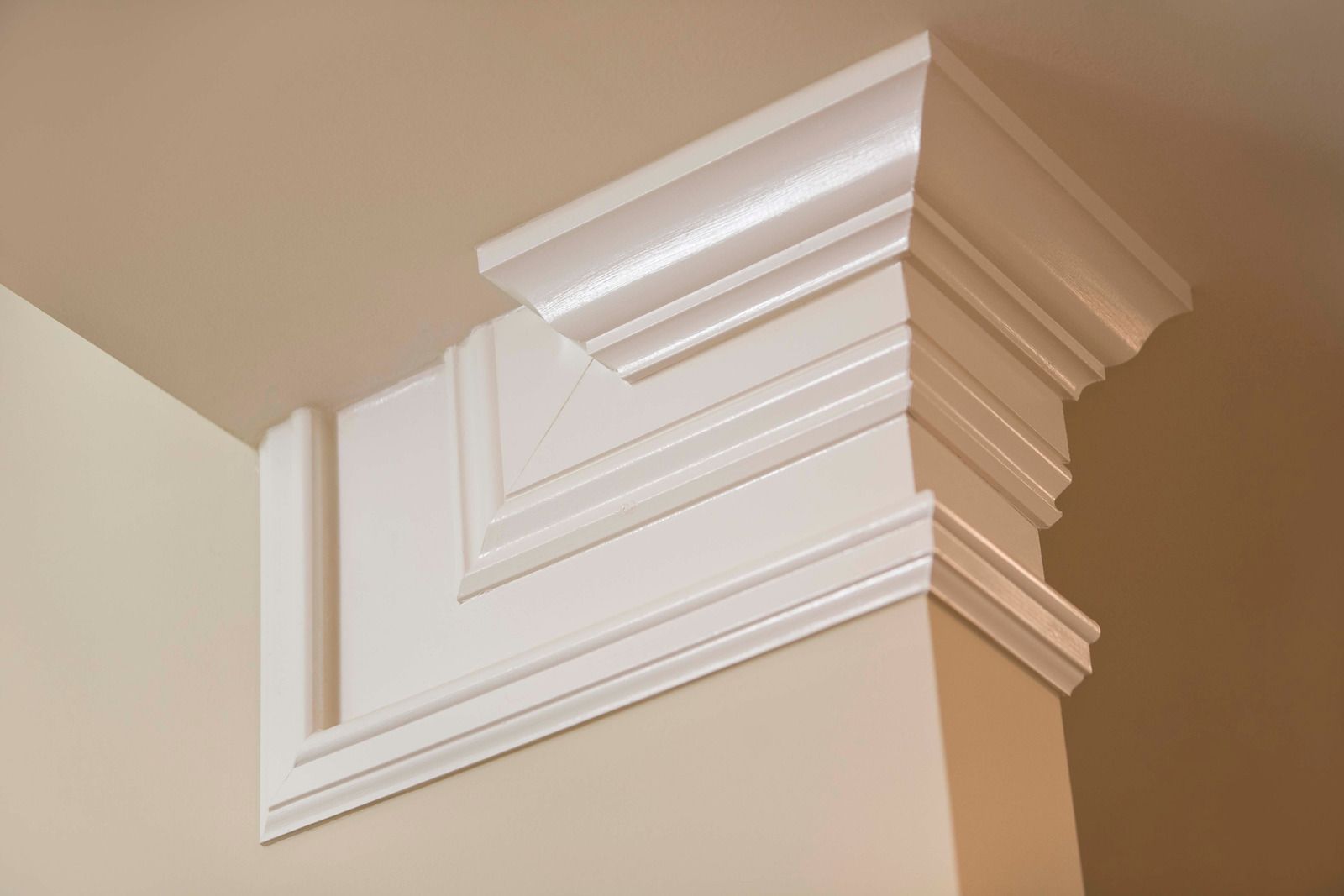 White crown molding corner with layered geometric details on a beige wall.