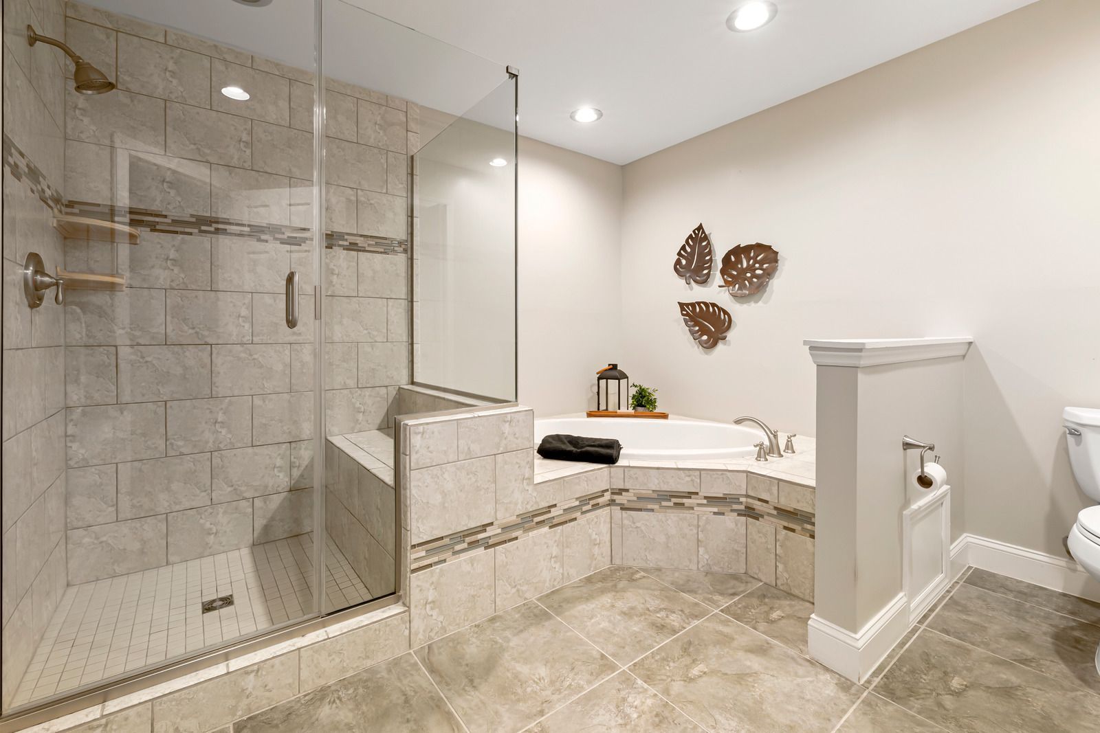 Bathroom with a tiled walk-in shower, corner jacuzzi tub, and a toilet. Beige tiles and walls.