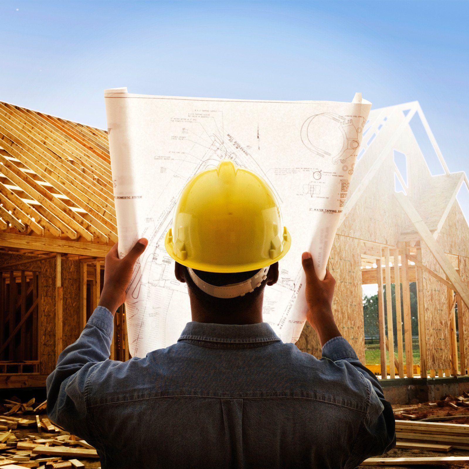 Construction worker in yellow helmet examines blueprints at a building site.