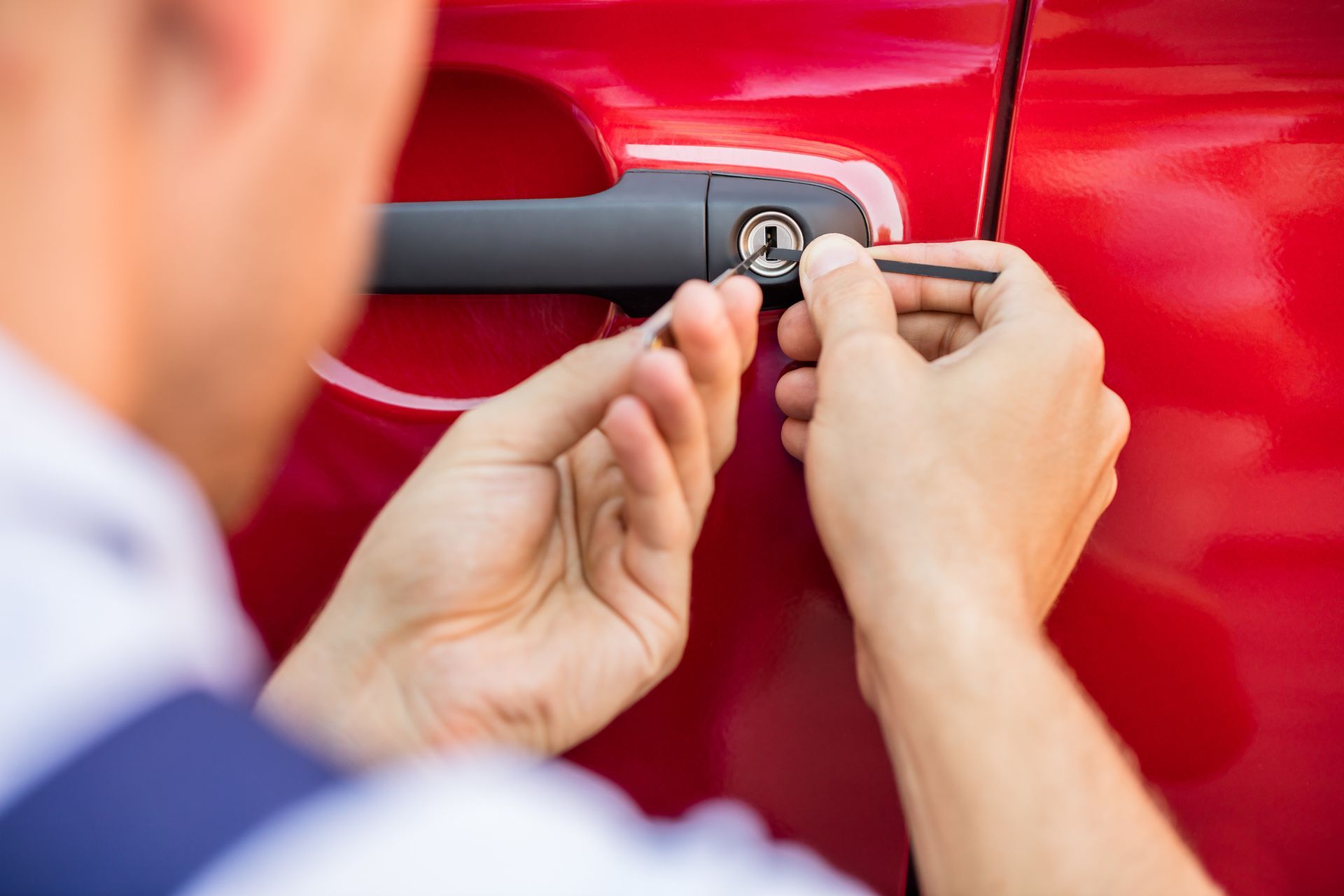 Person using lock picks to unlock a red car door.
