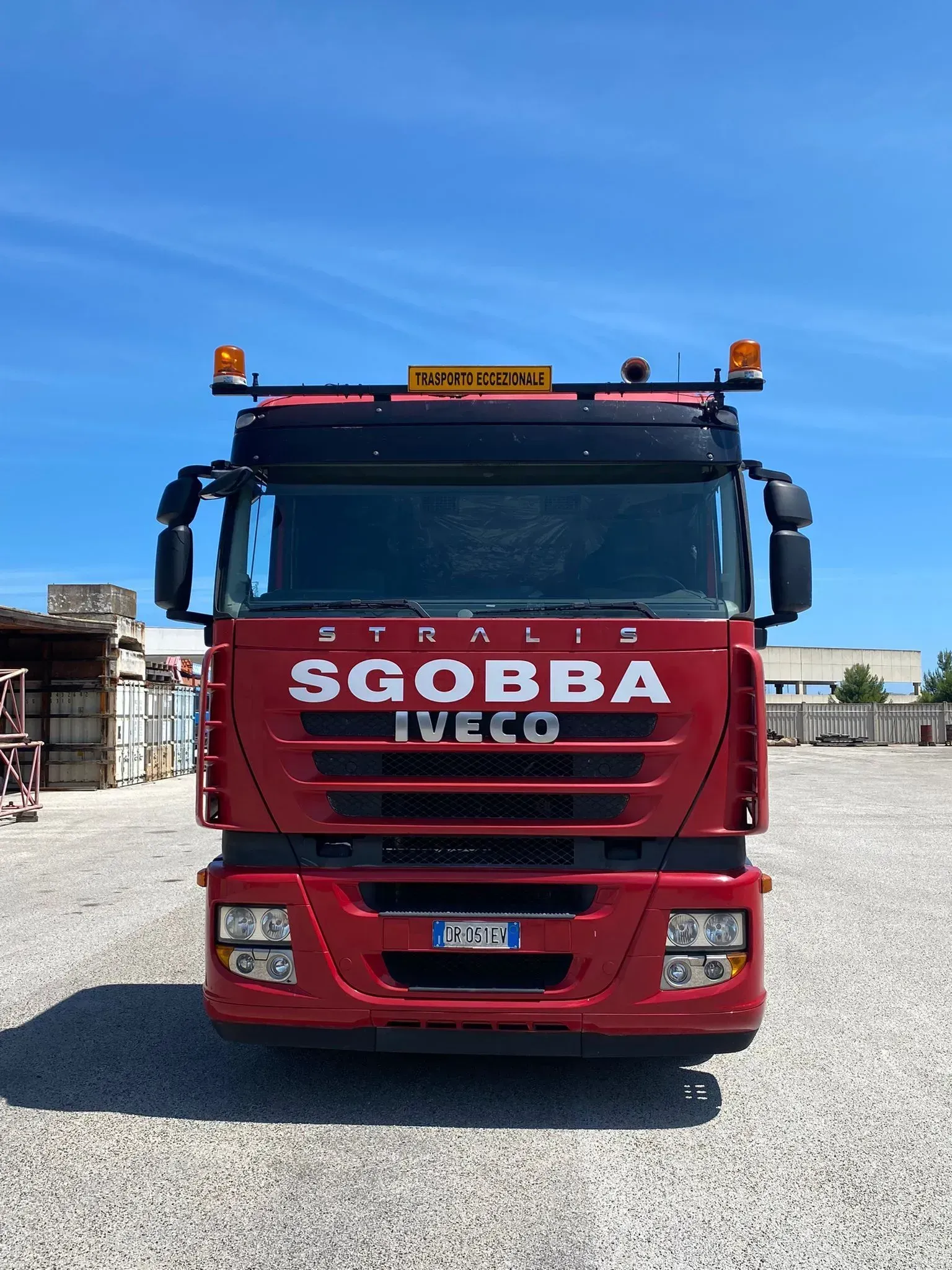 Camion Scania rosso con il logo SGOBBA parcheggiato su un piazzale ghiaioso sotto un cielo azzurro e limpido.