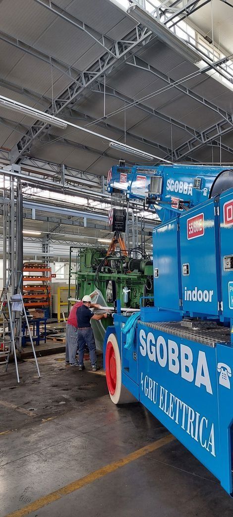 Un camioncino blu di servizio all'interno di un cantiere coperto, con operai e coni stradali arancioni nelle vicinanze.