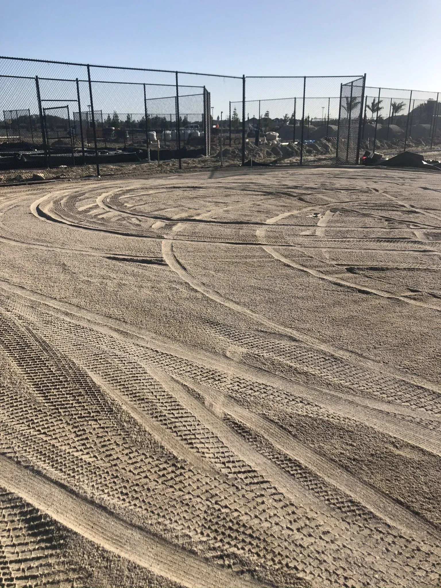 Empty dirt lot with tire tracks and chain-link fencing under a clear sky