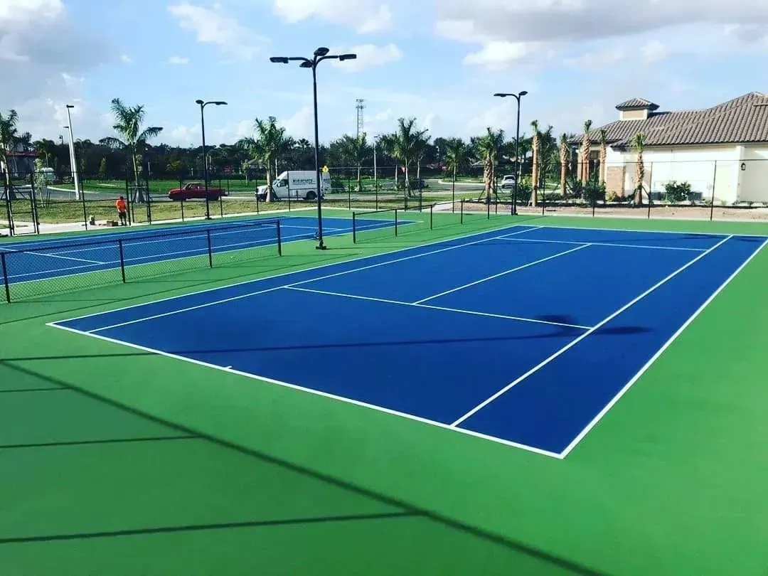 Blue outdoor tennis court with green borders and white lines under a clear sky