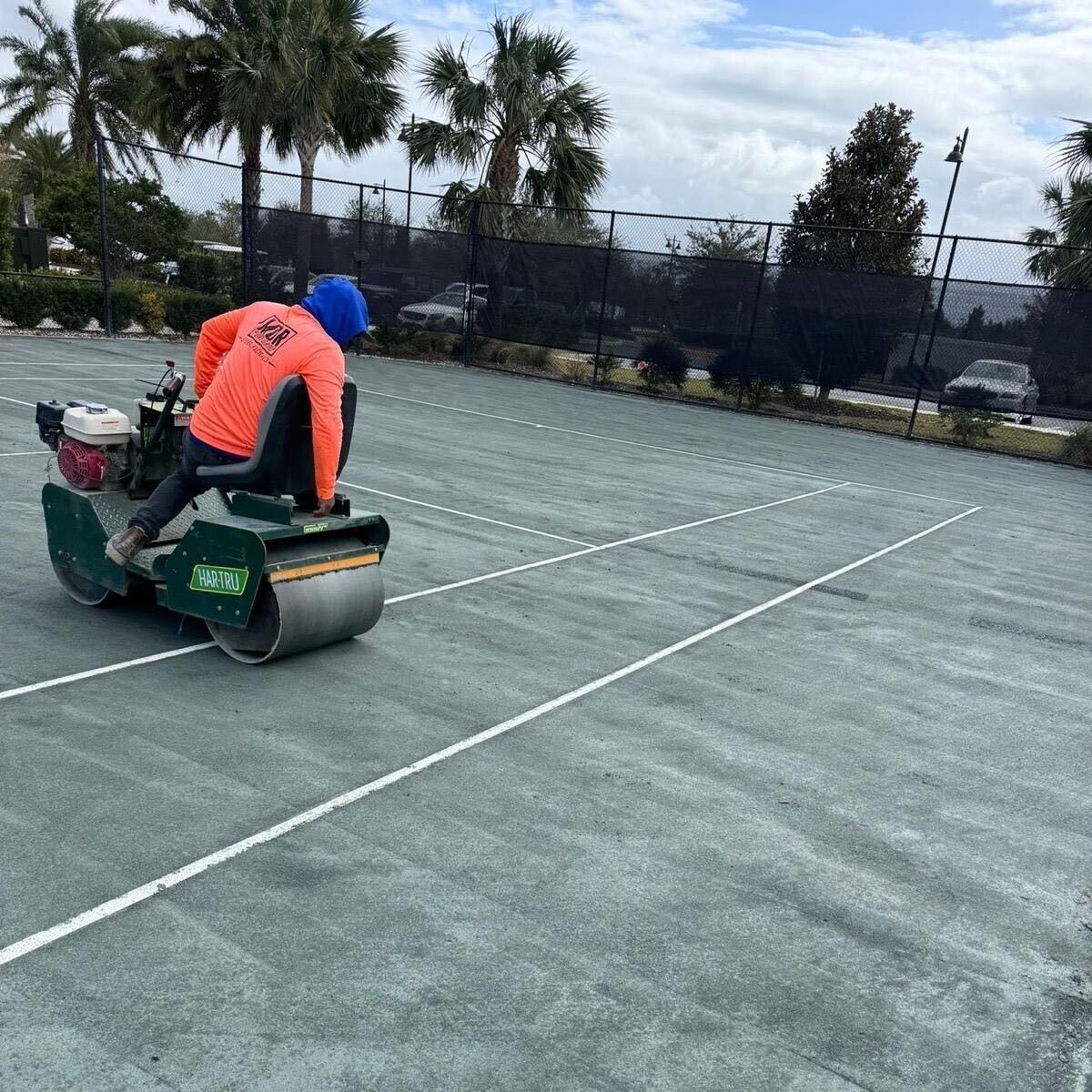 Worker riding a line striping machine on a tennis court, painting white court lines