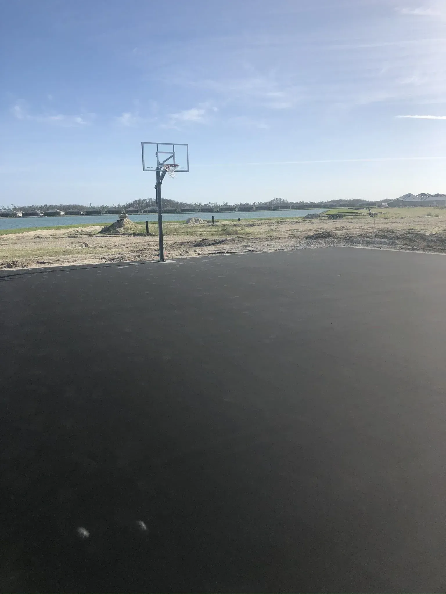 Outdoor basketball hoop beside a rocky shoreline under a clear blue sky