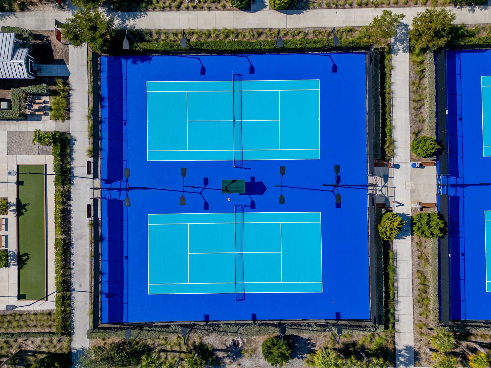 Aerial view of a blue tennis court with four players and surrounding greenery