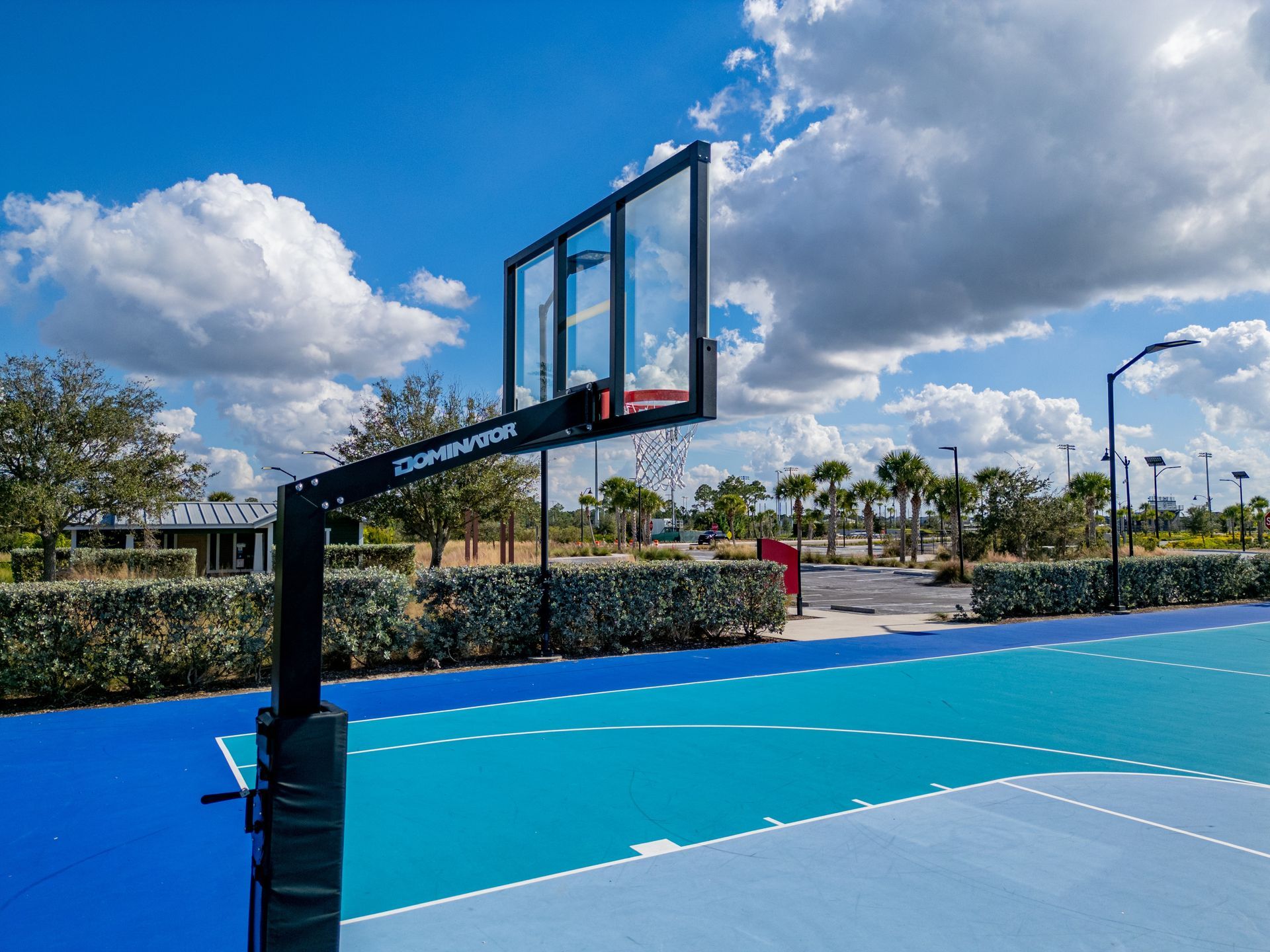 Outdoor basketball court with blue surface and a hoop under a bright cloudy sky