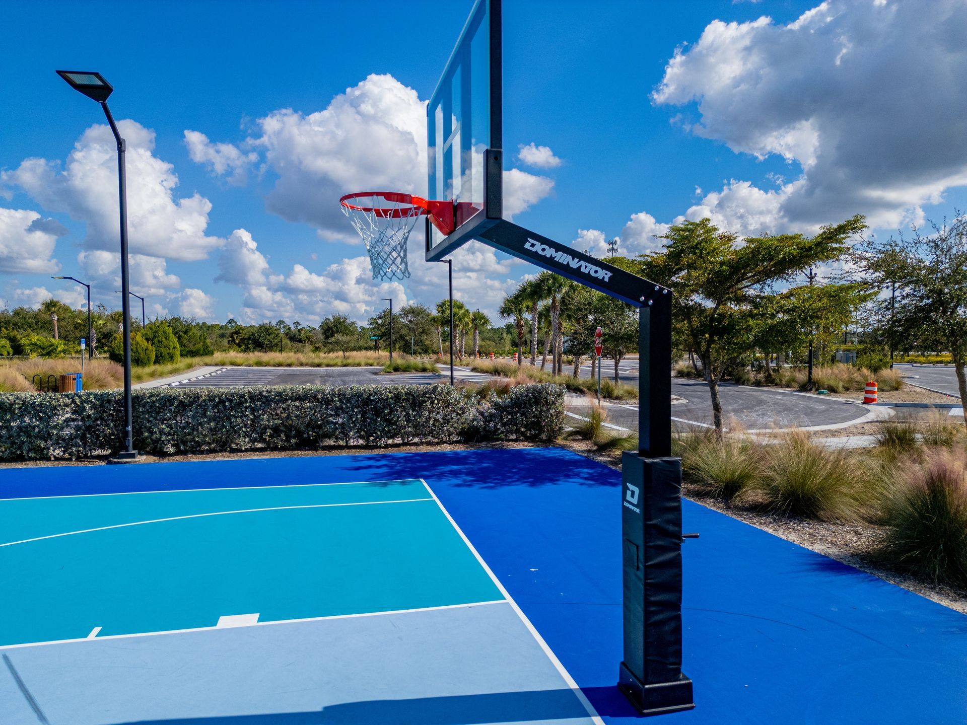 Outdoor basketball court with a black hoop, blue surface, and cloudy sky beyond the fence