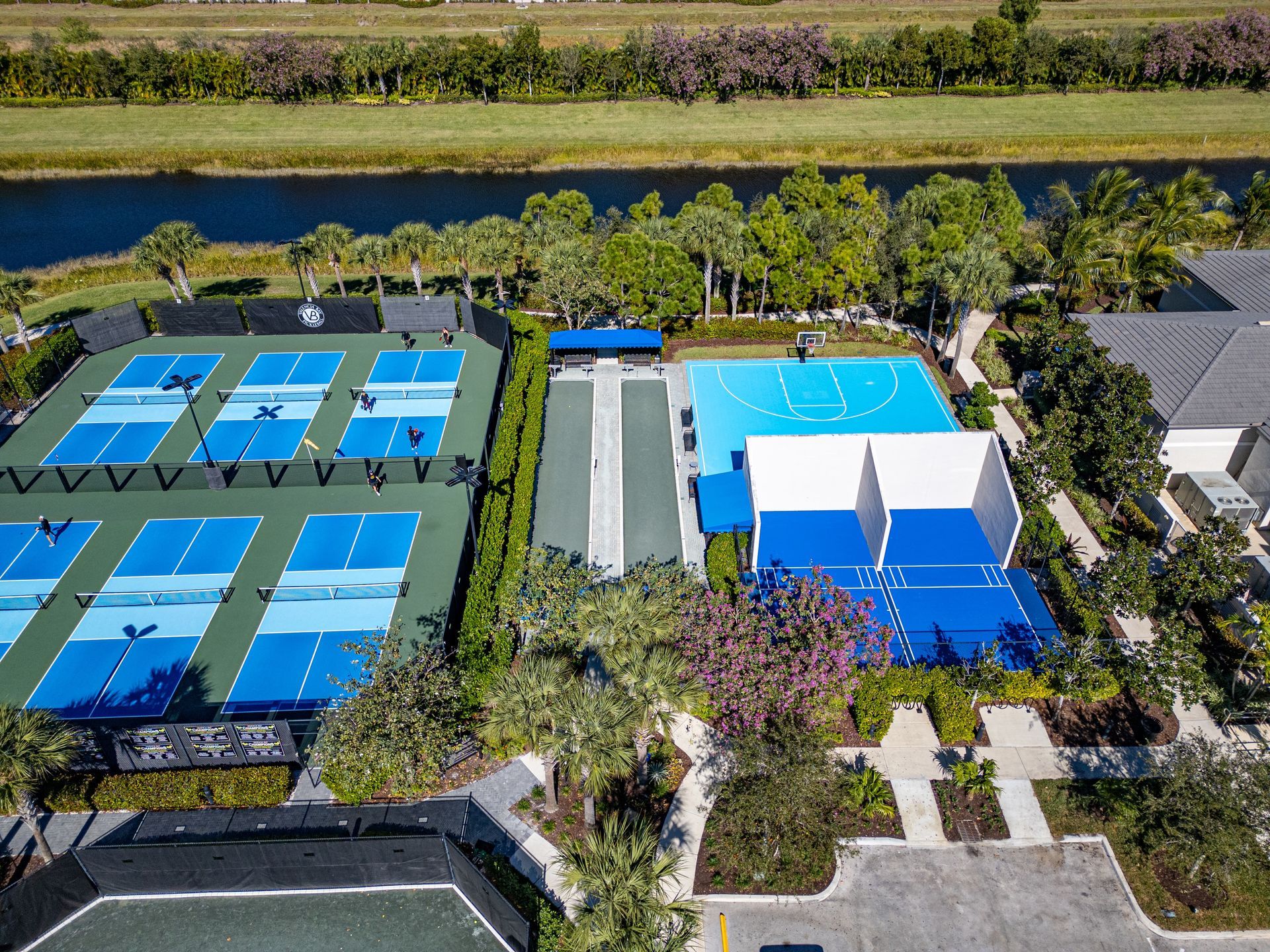 Aerial view of multiple clay tennis courts with a few players and surrounding trees.