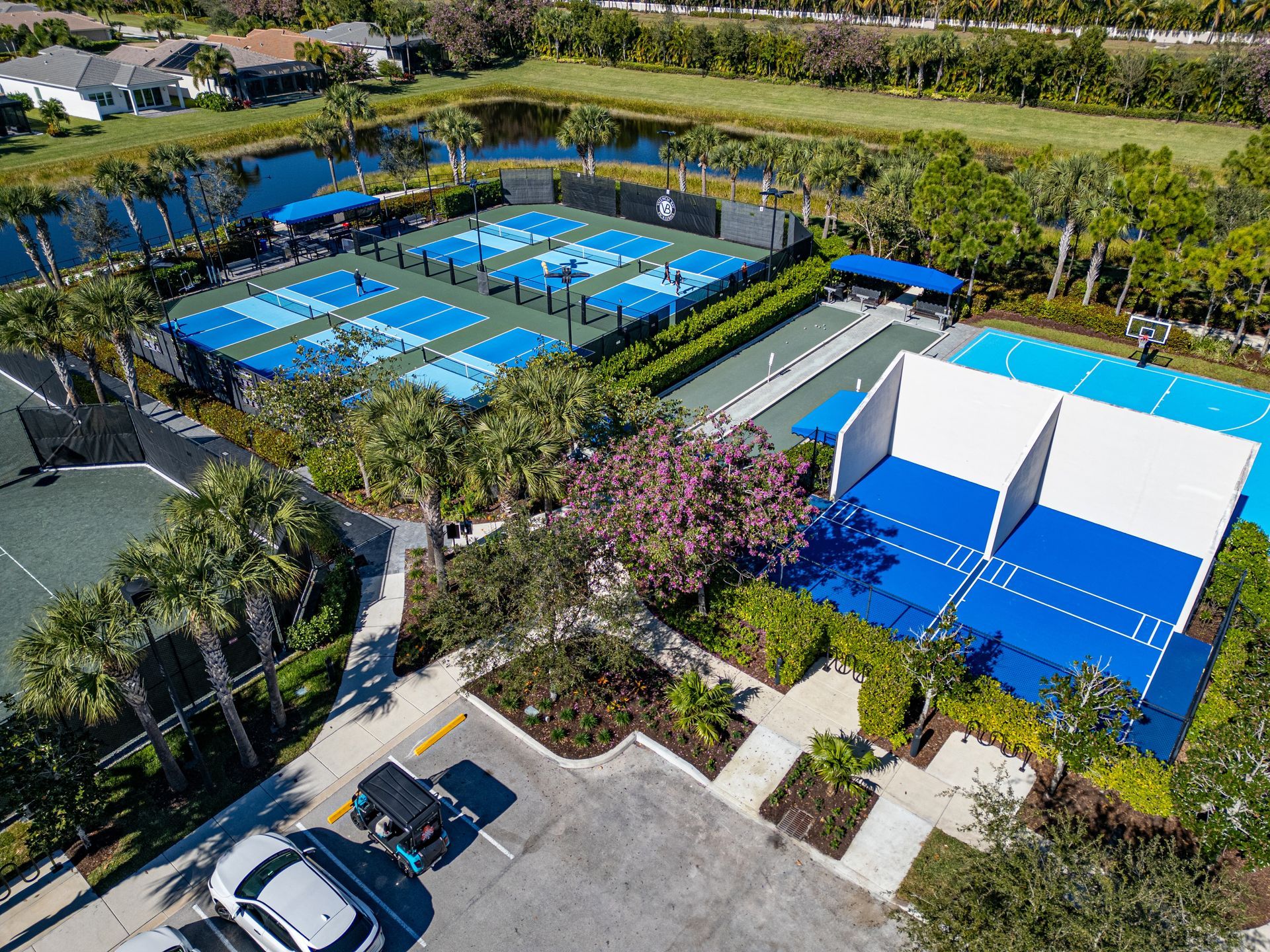 Aerial view of blue tennis courts and a pool area surrounded by trees and buildings