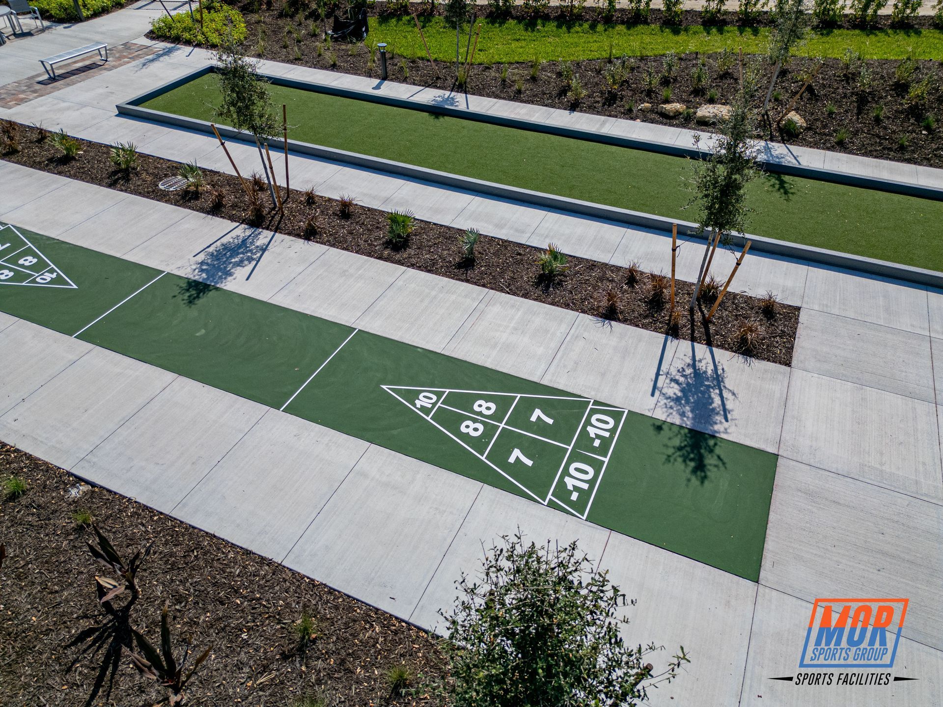 Outdoor shuffleboard courts with green playing surfaces, white markings, and surrounding landscaping.