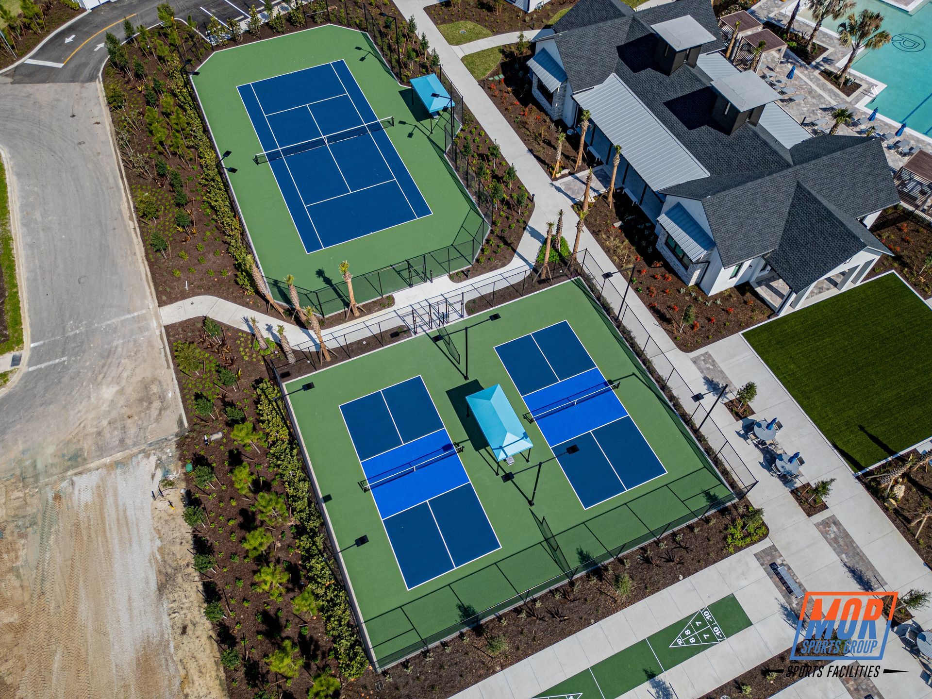 Aerial view of a sports complex with two blue tennis courts and a larger blue court beside a building.
