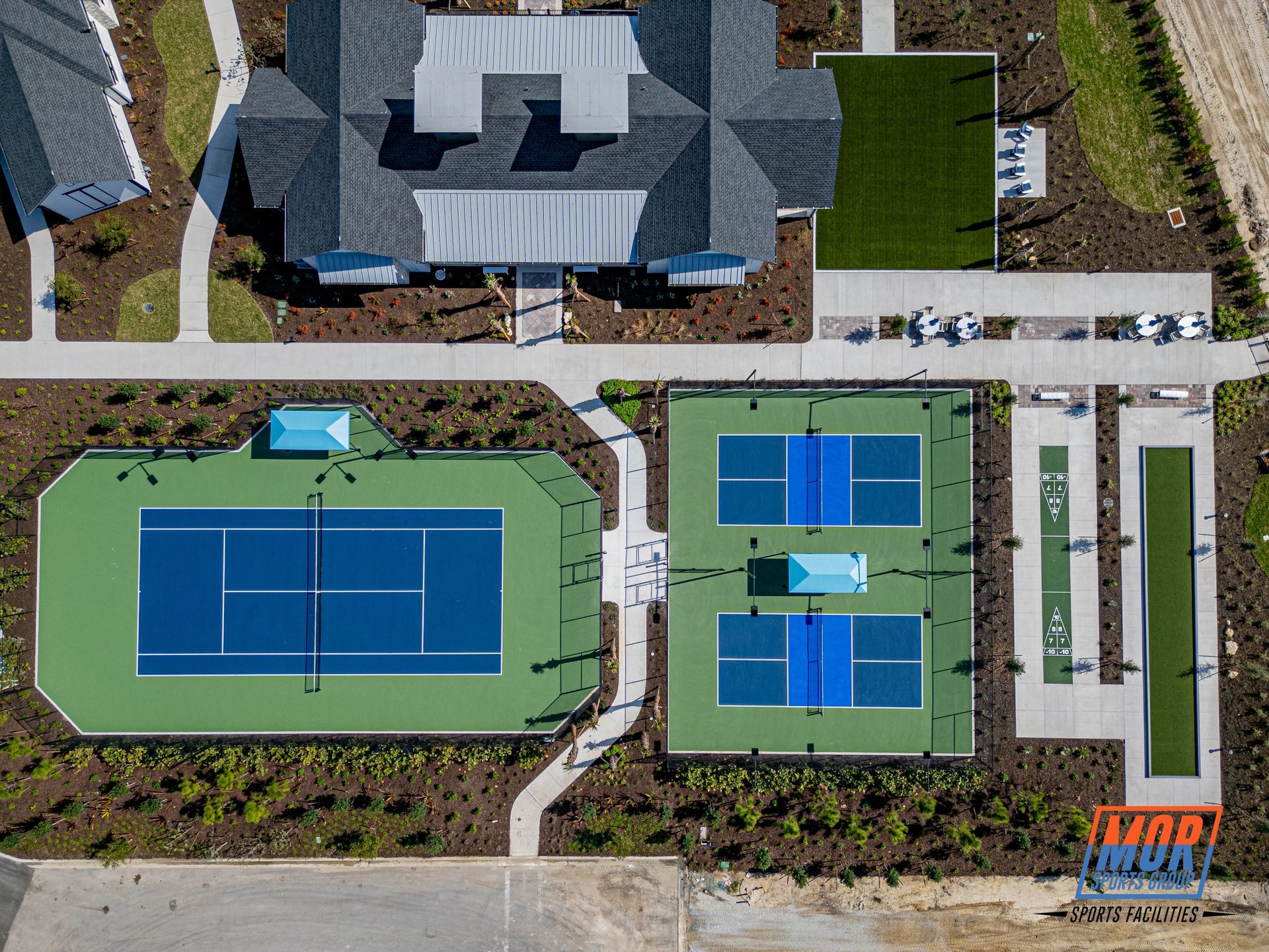 Aerial view of a house with two blue tennis courts and landscaped walkways.