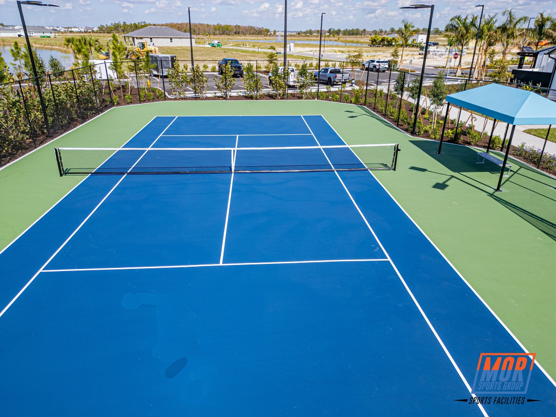Empty blue tennis court with green sidelines, net, and a beachside resort in the background