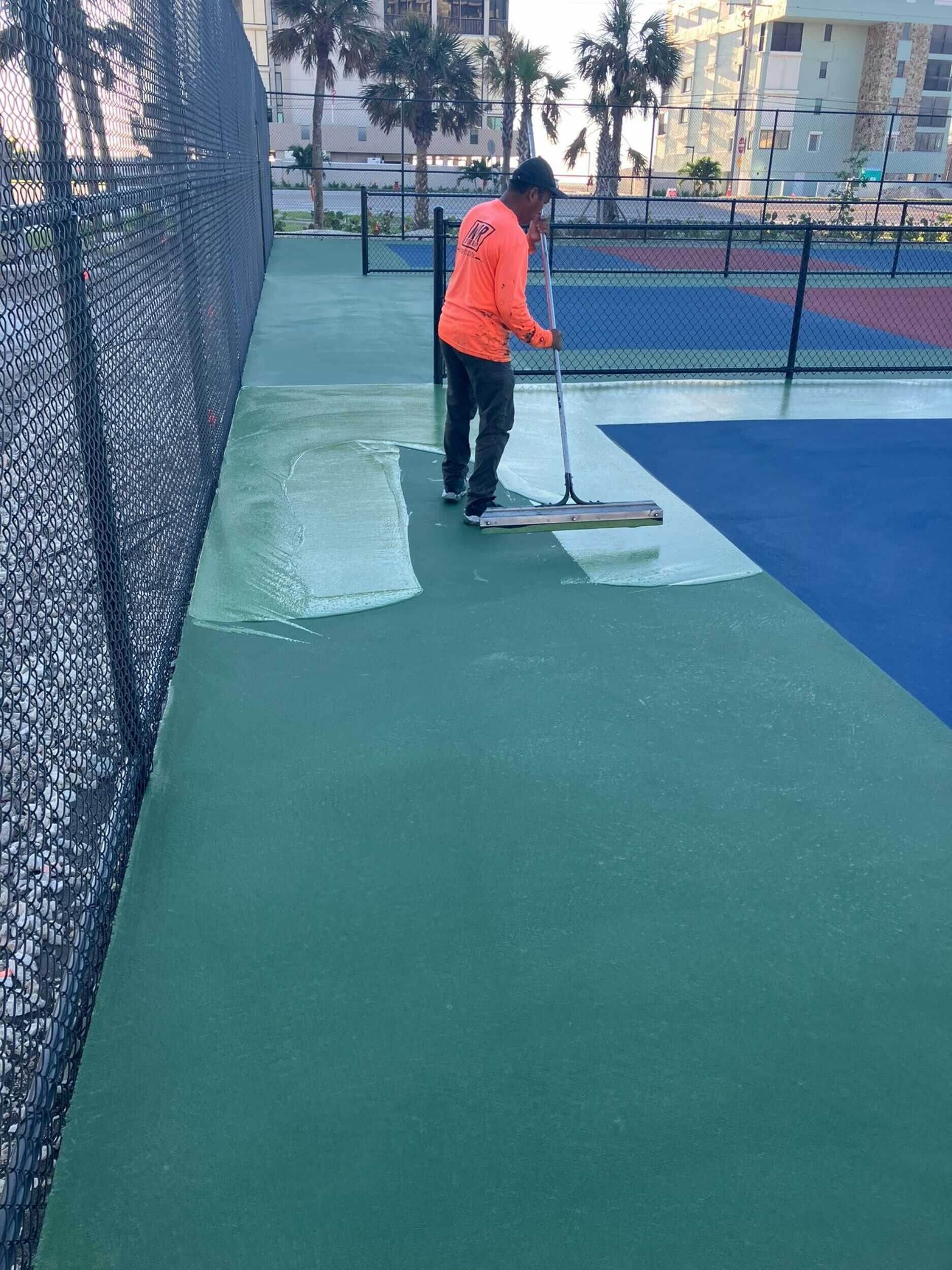 Person in an orange jacket painting court lines on an outdoor tennis court.