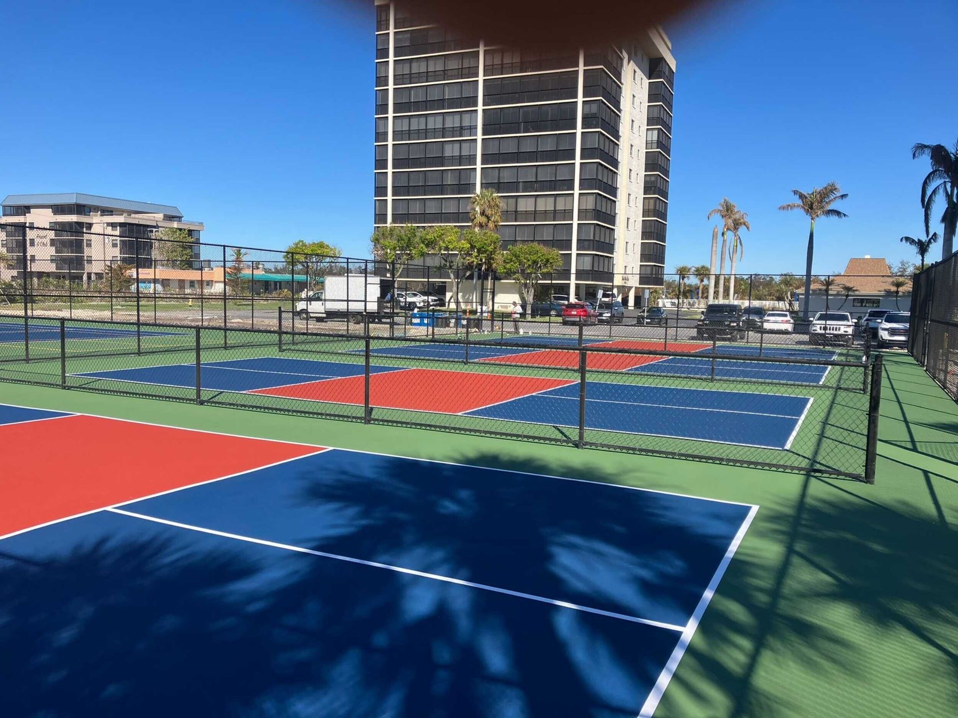 Colorful pickleball courts by the beach with a tall building and palm trees in the background