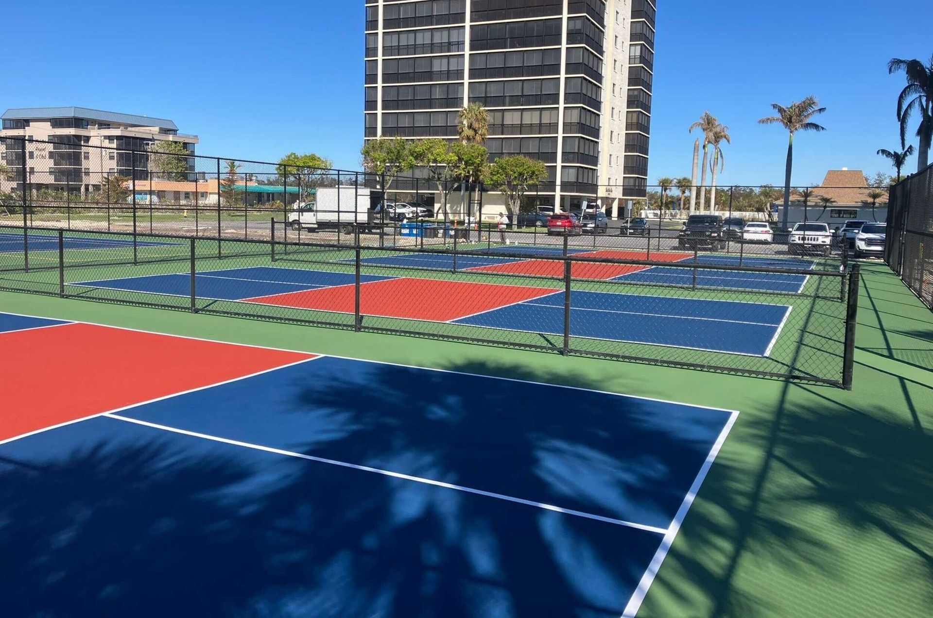 Colorful outdoor pickleball courts beside a waterfront high-rise under a clear blue sky