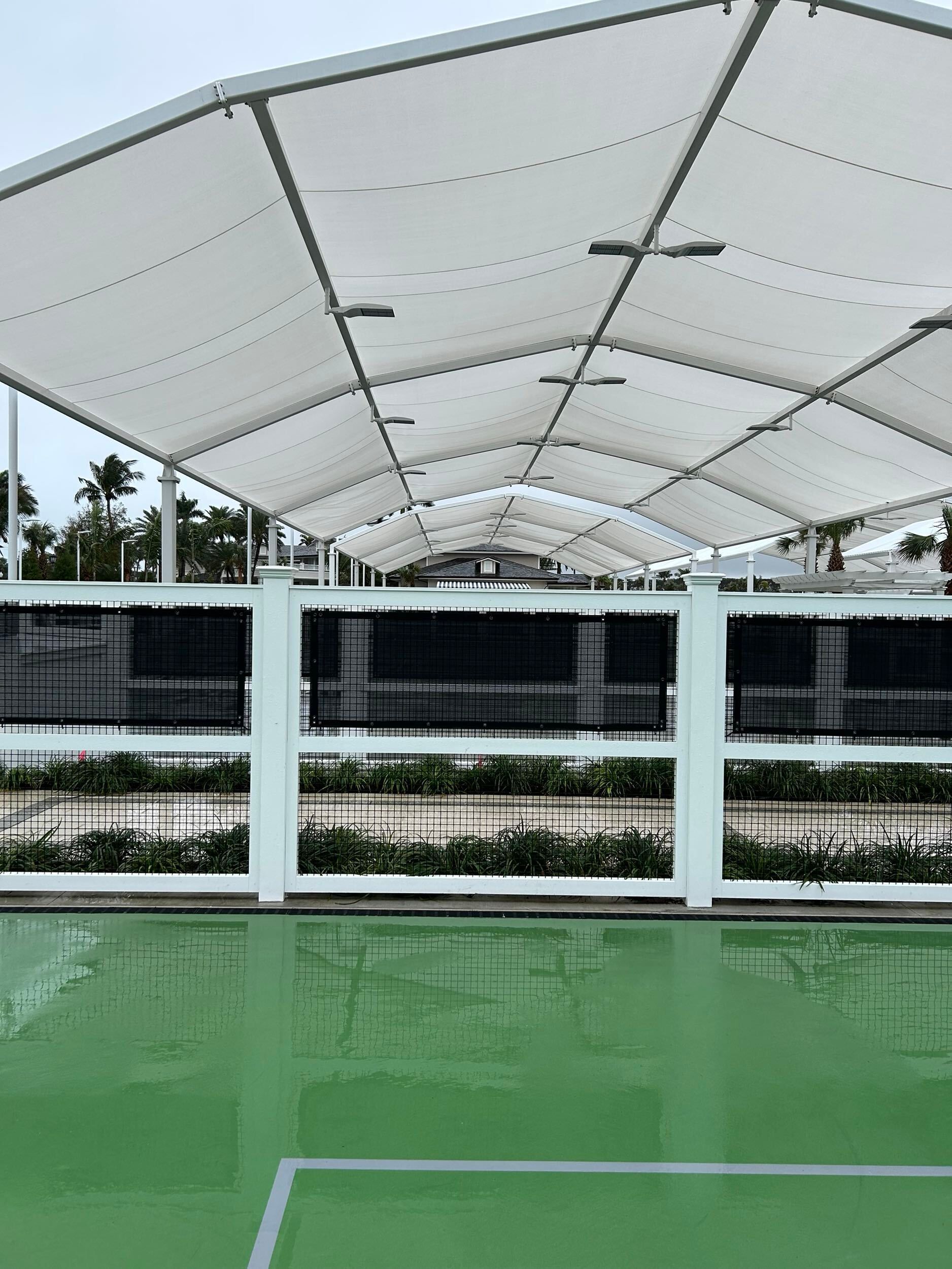 Covered tennis court with a white canopy, black fencing, and a green playing surface