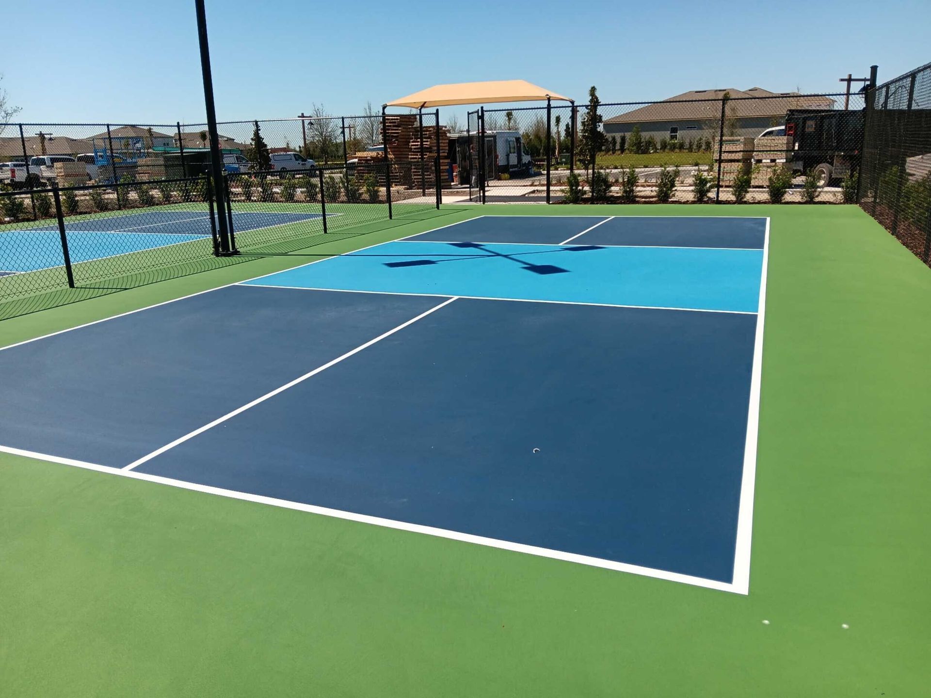 Outdoor blue-and-green pickleball court beside a swimming pool under a clear sky