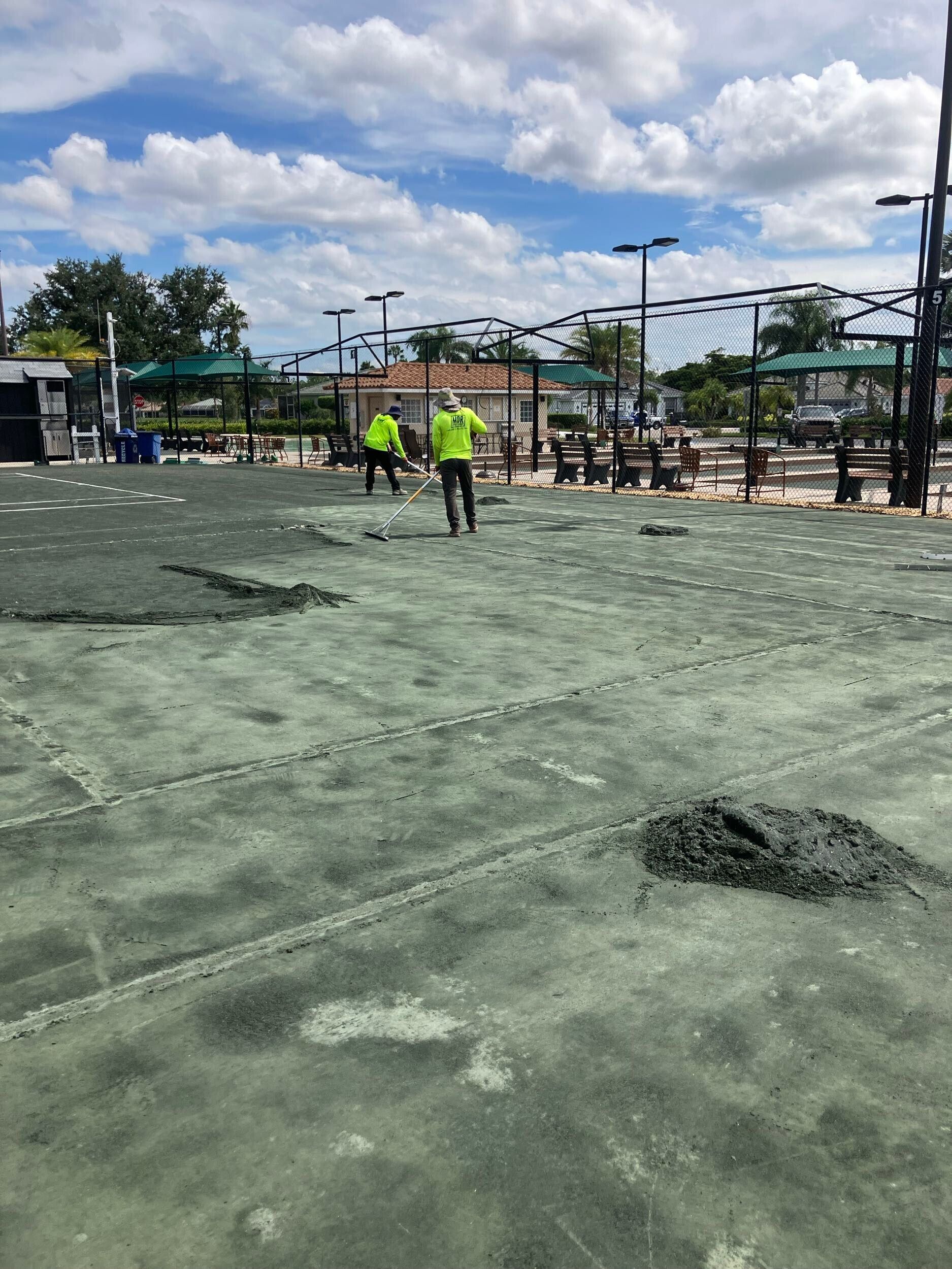 Workers smoothing a large gray concrete slab at a construction site under a cloudy sky