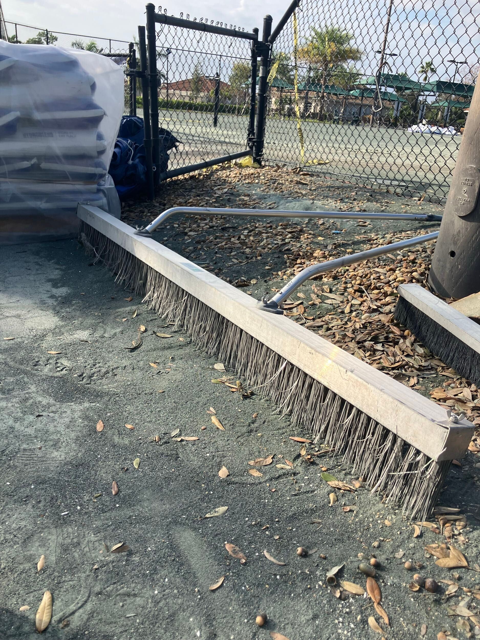 Outdoor gravel area with raised border, chain-link fence, and tarped items beside a tree