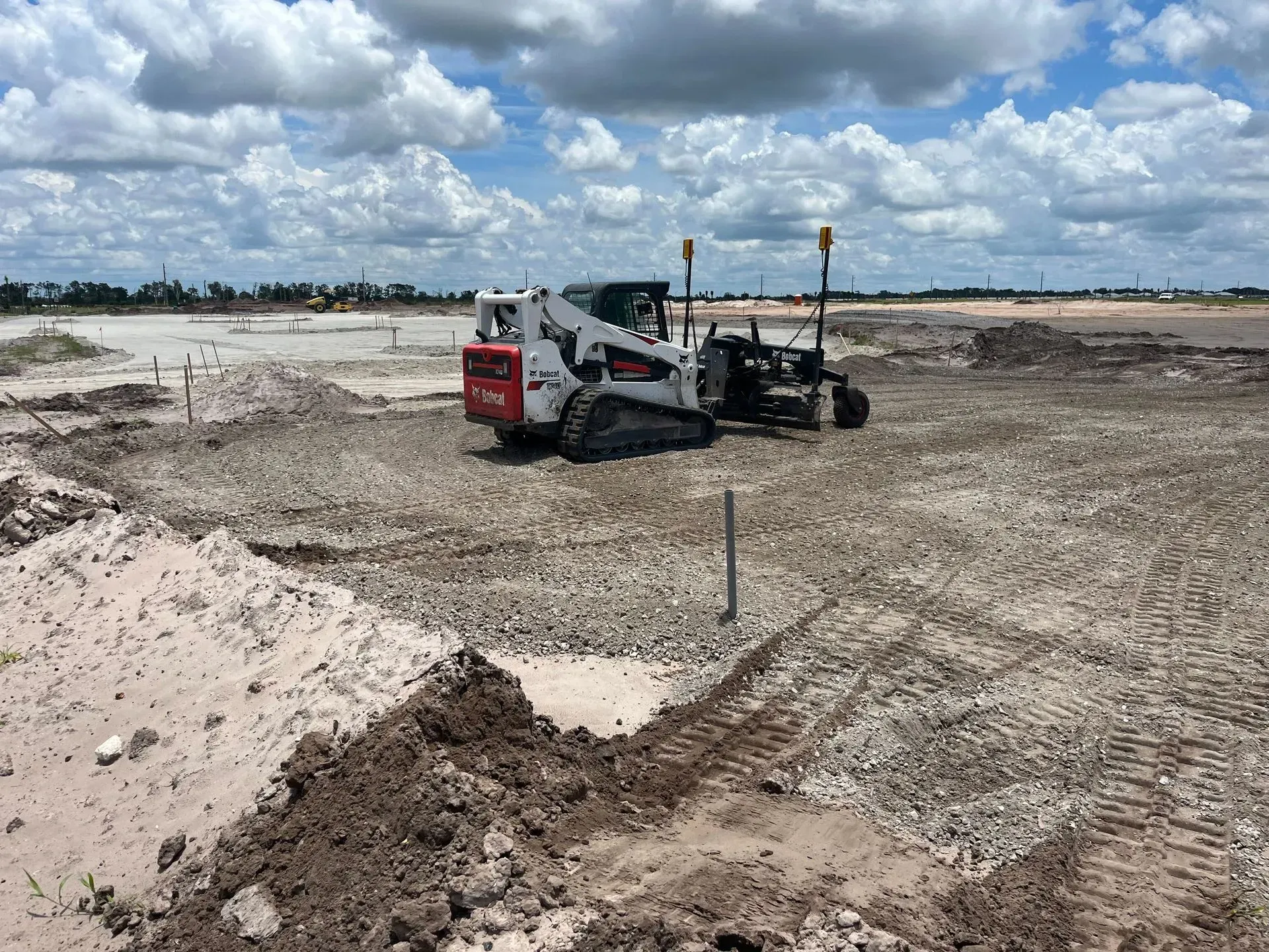 Construction vehicle grading dirt on a cloudy, open work site