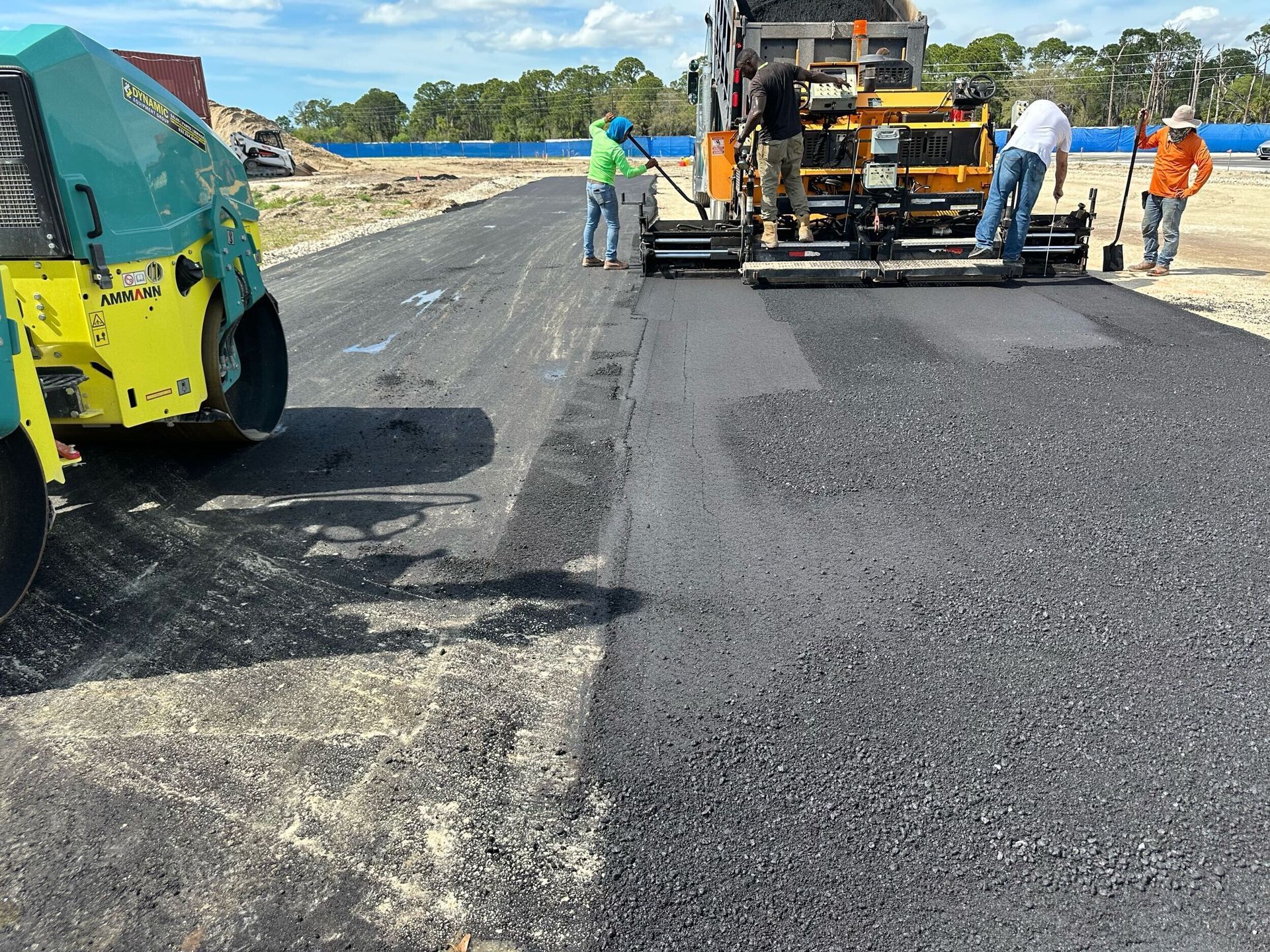 Road paving crew with asphalt paver and roller resurfacing a highway under a bright sky