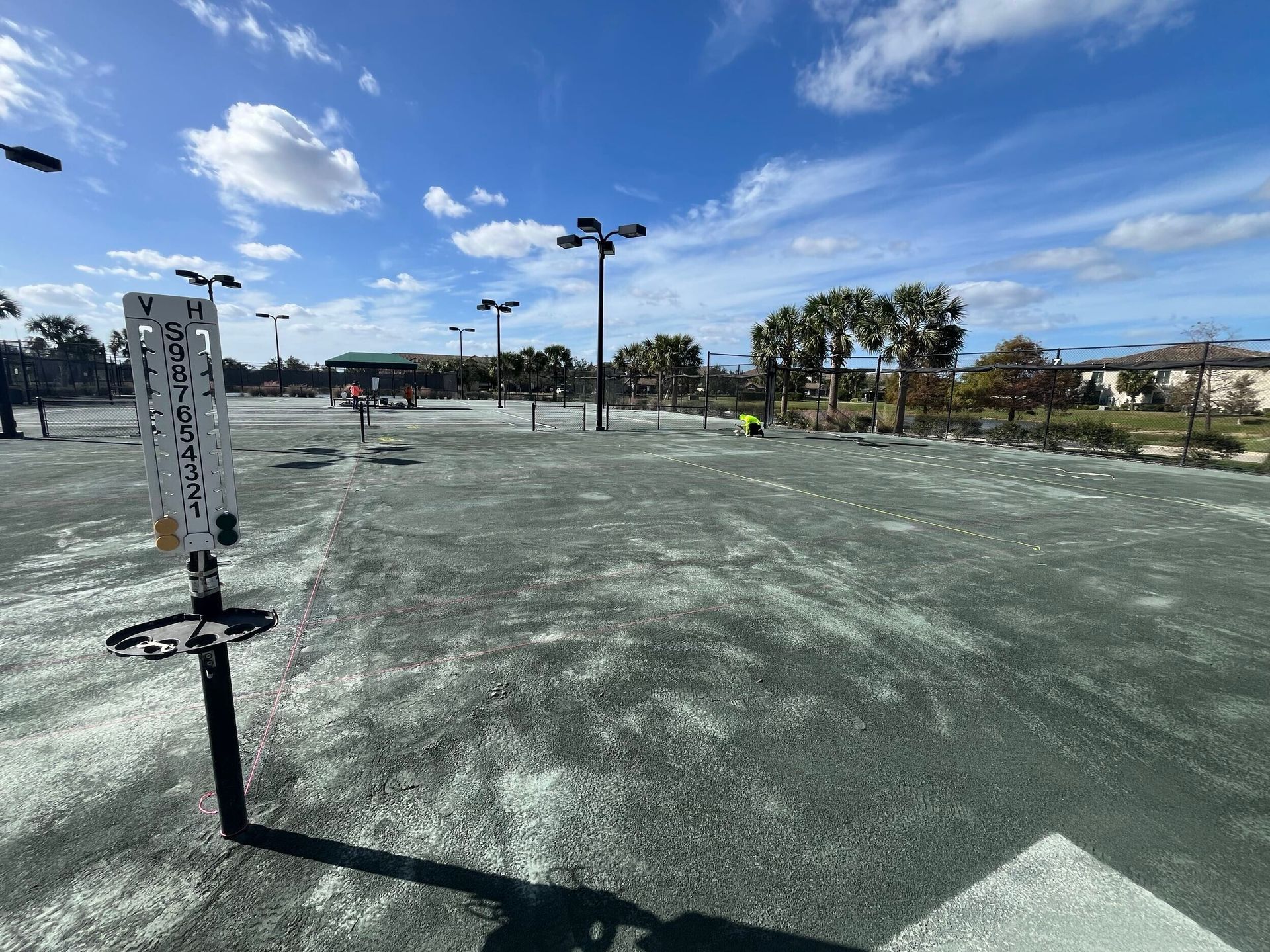 Empty outdoor skatepark under a bright blue sky, with light poles and palm trees in the distance