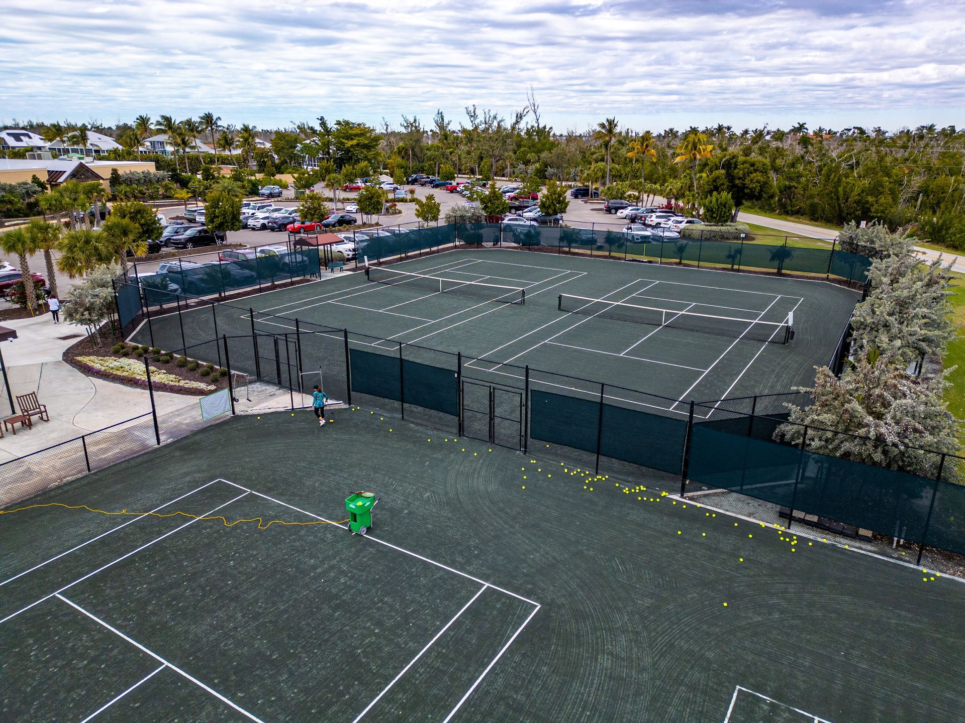 Empty green sports courts surrounded by fencing and trees under a cloudy sky