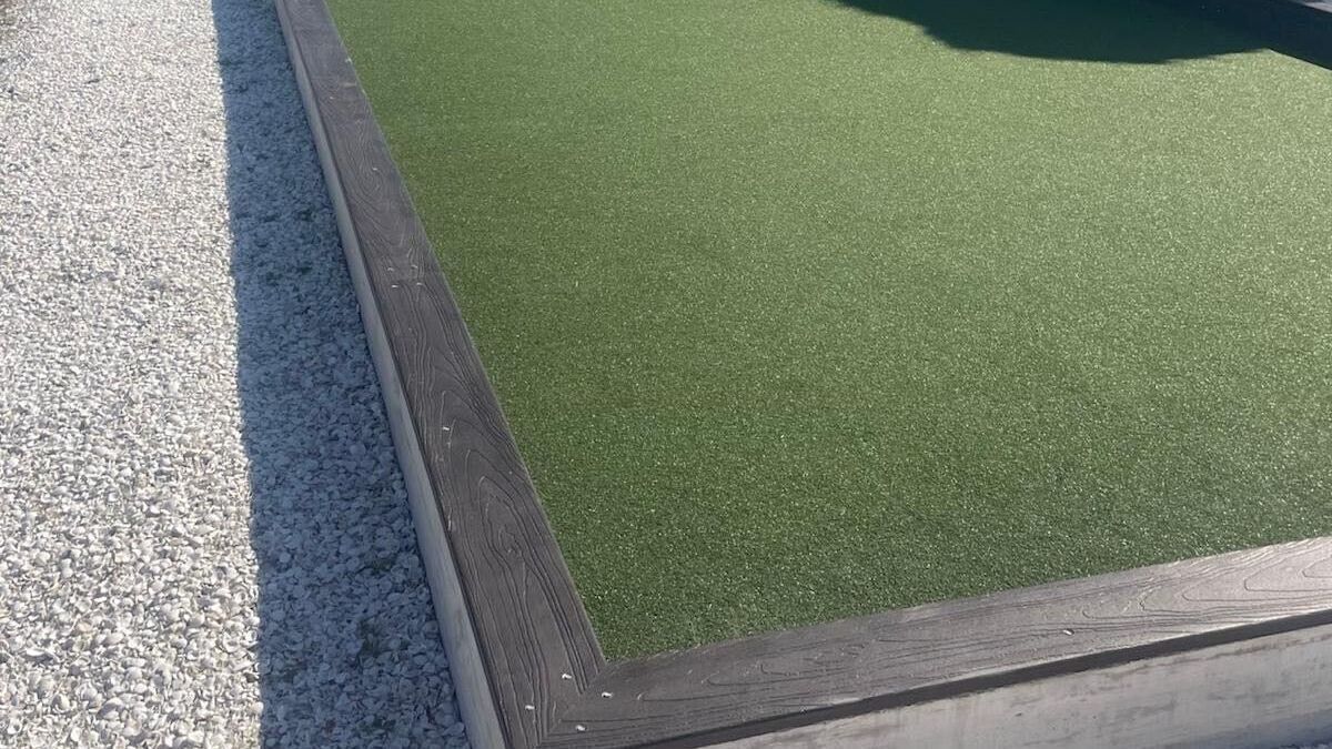 Raised planter box with green artificial turf and gray gravel beside it