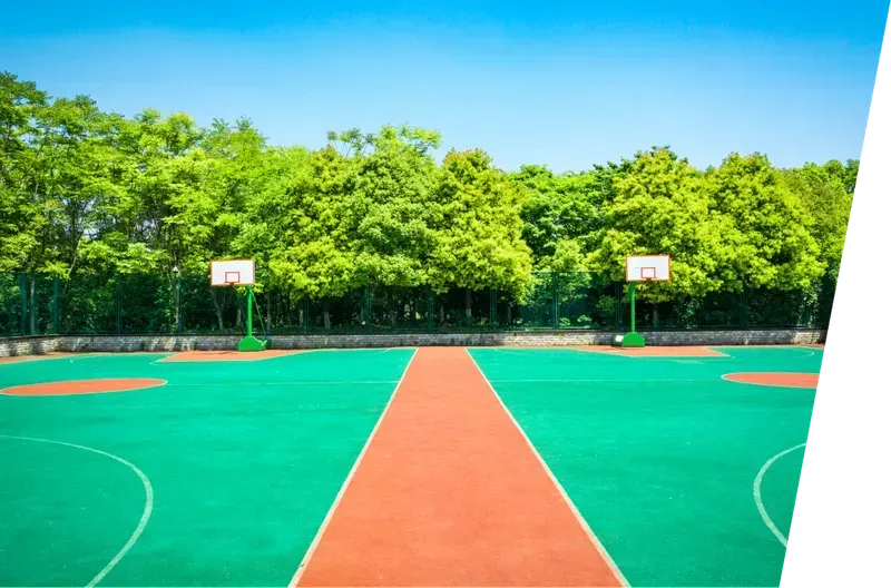 Empty outdoor basketball court with bright green and orange pavement and trees in the background