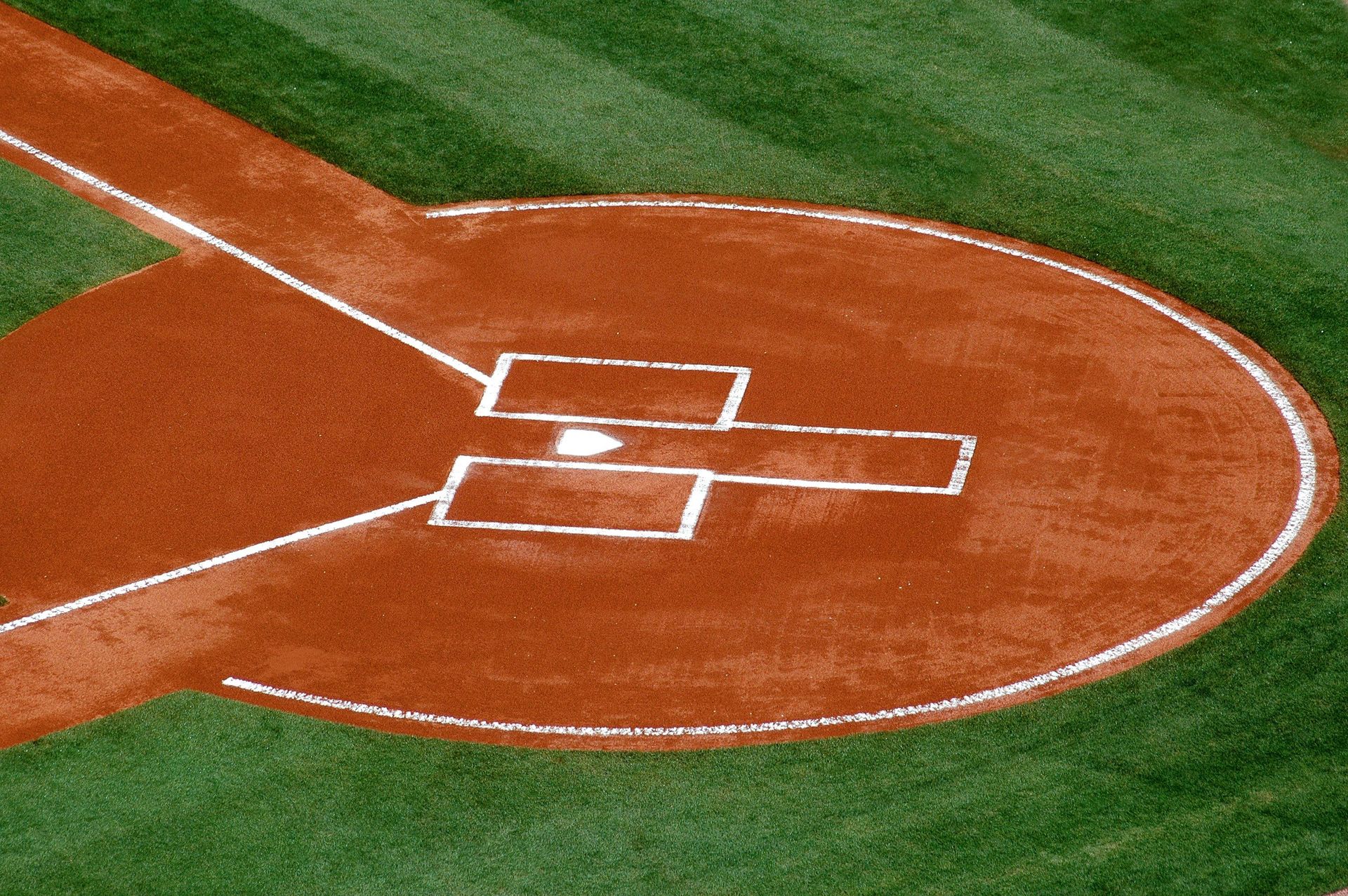 Baseball field with players on the diamond, empty bleachers, and a clear blue sky
