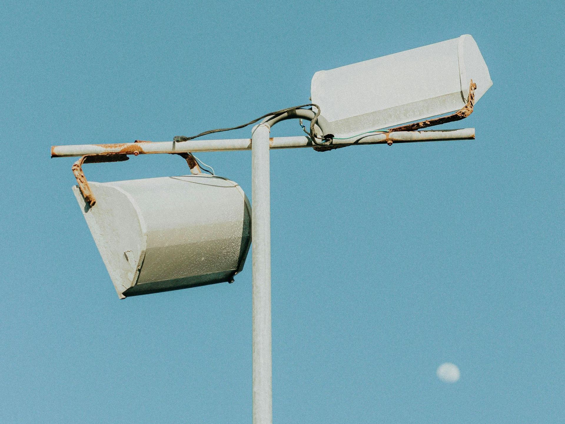 Two white speakers mounted on a pole against a blue sky