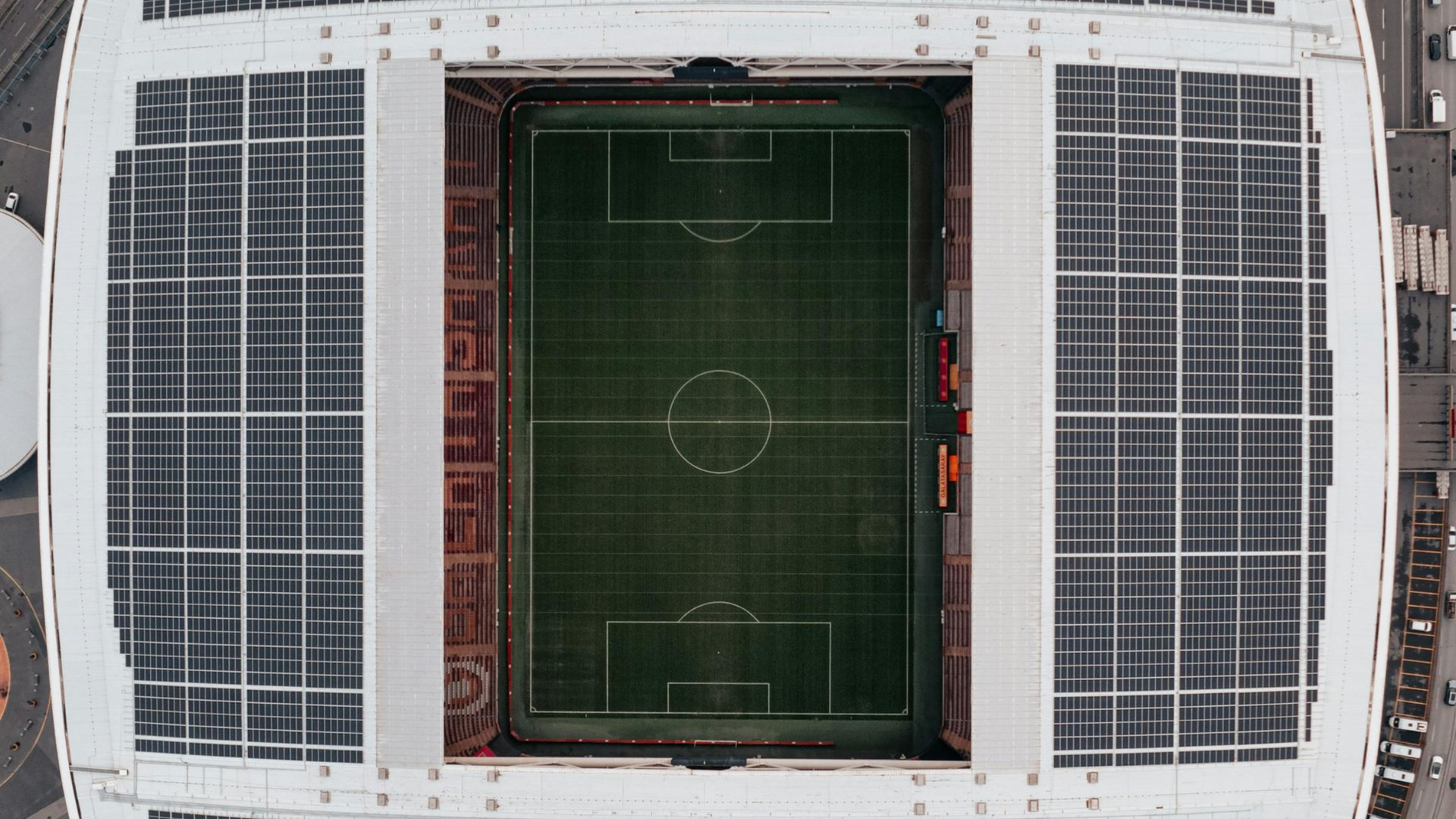 Aerial view of a soccer stadium with a green field and surrounding solar-panel roof sections