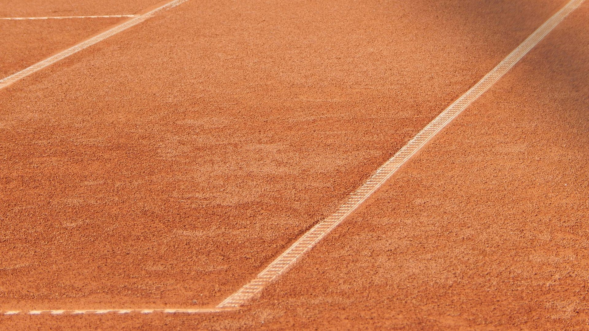 Orange clay tennis court with white boundary lines in close-up view