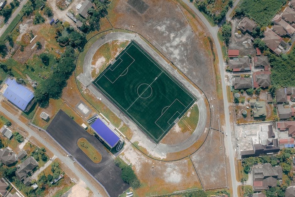Aerial view of a soccer field surrounded by a running track and buildings in a neighborhood