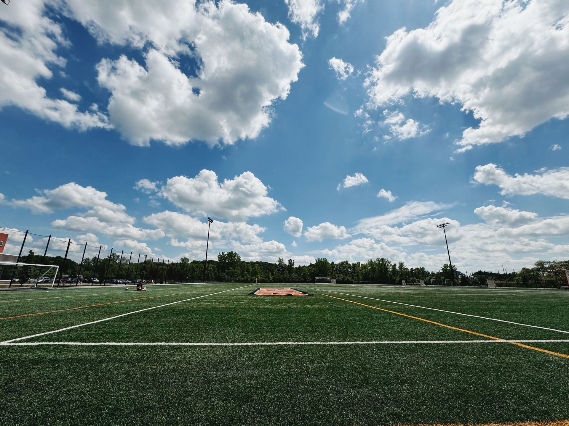 Wide view of empty soccer field under a bright blue sky with scattered clouds